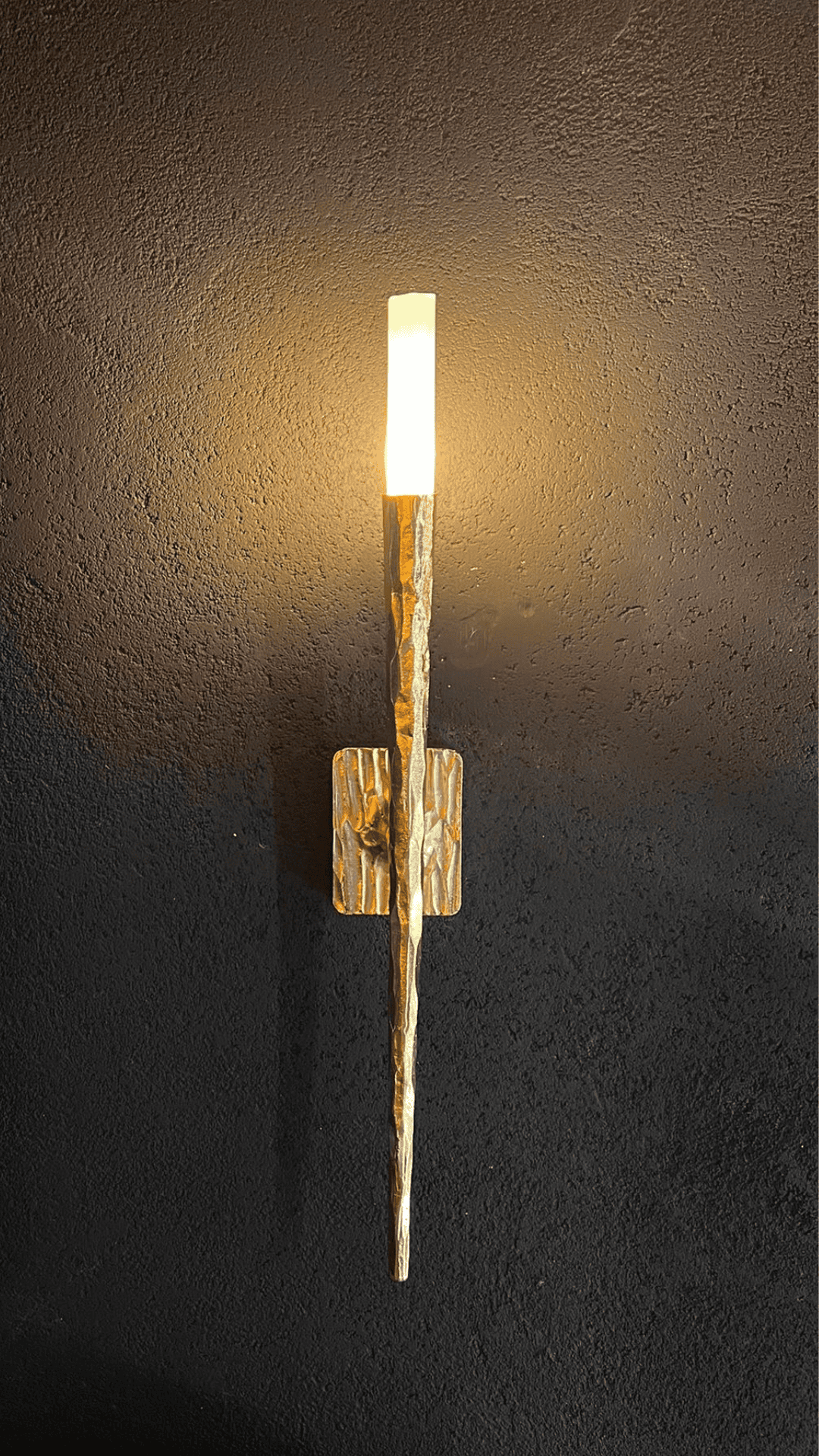 Gold sculpted wall sconce casting warm light on a matte black textured surface.