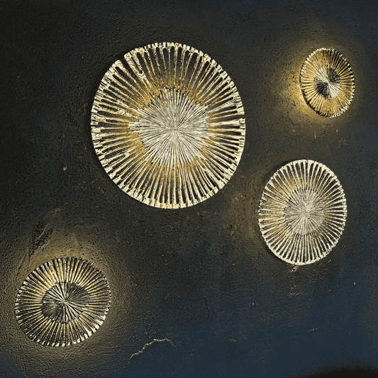 Set of four round cast aluminum wall sconces in sunburst design with gold, nickel, aged brass and black finishes on a dark textured wall