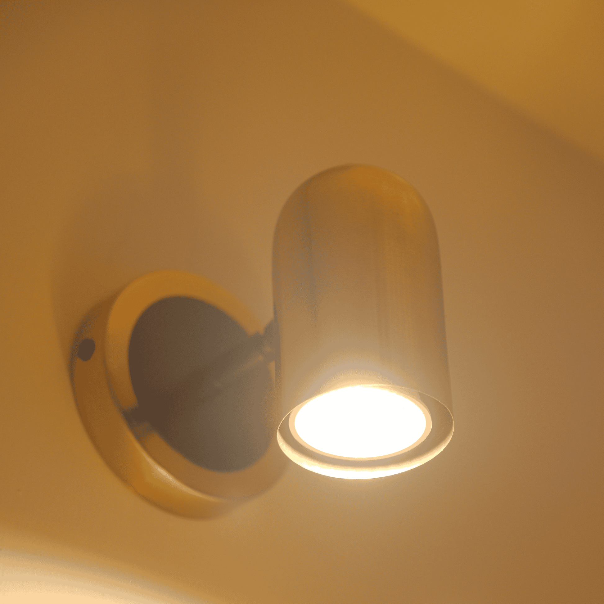 Adjustable brass wall sconce emitting a warm LED beam in a minimalist setting.