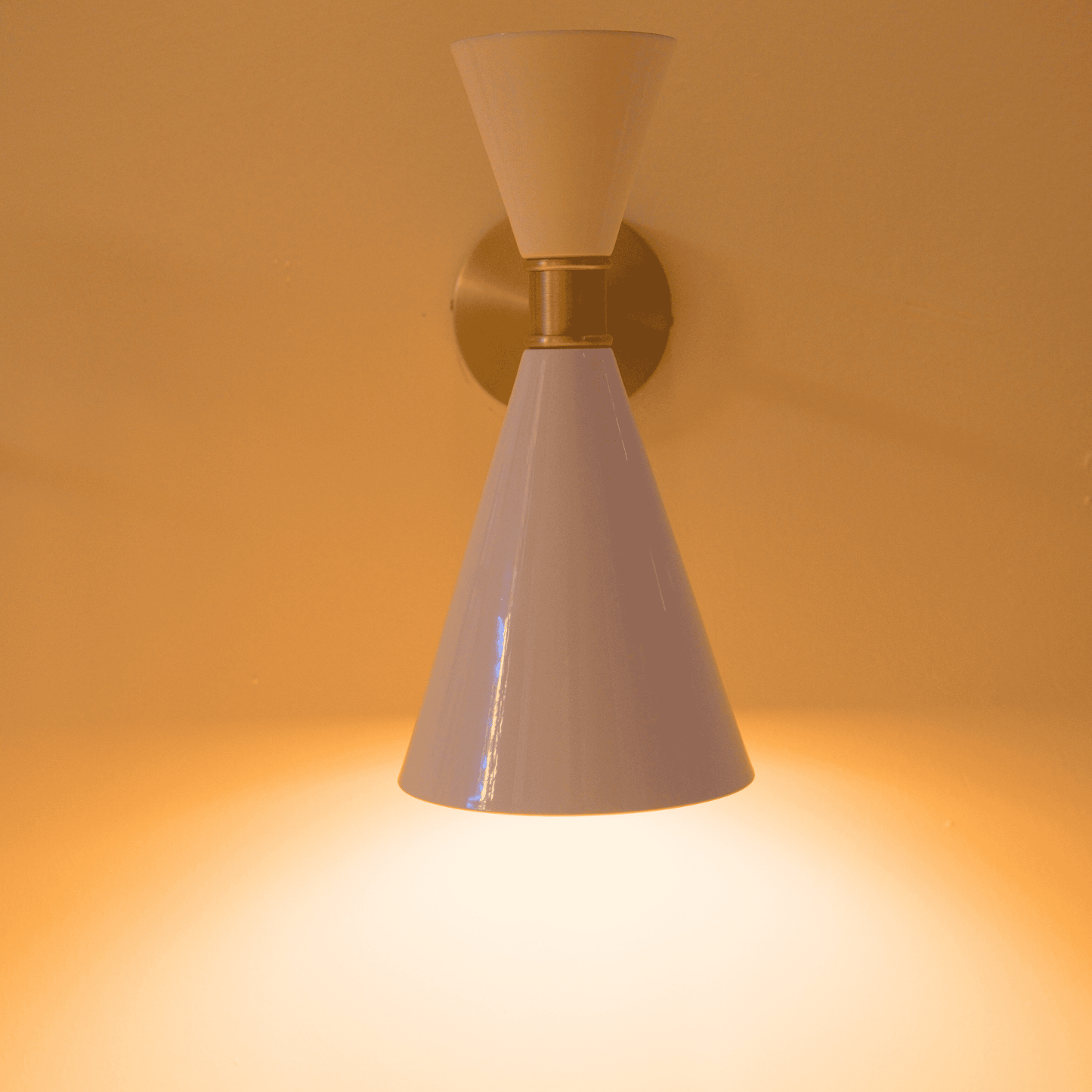 Adjustable white and brass wall sconce with double-cone shade and pivot arm for directional lighting.