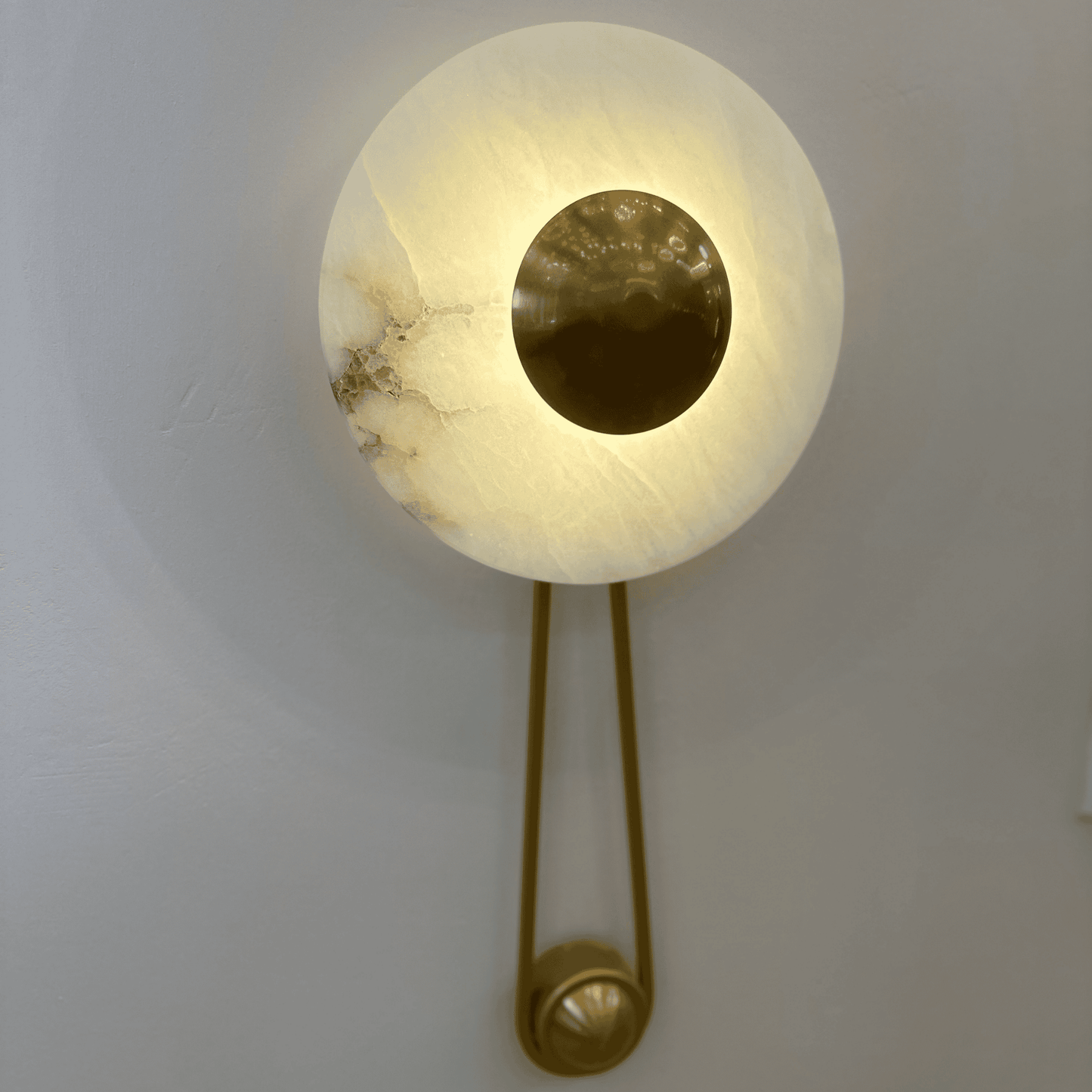 Alabaster wall sconce with brass disc mounted on a neutral-toned wall.