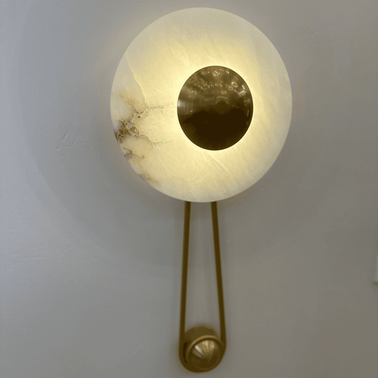Alabaster wall sconce with brass disc mounted on a neutral-toned wall.