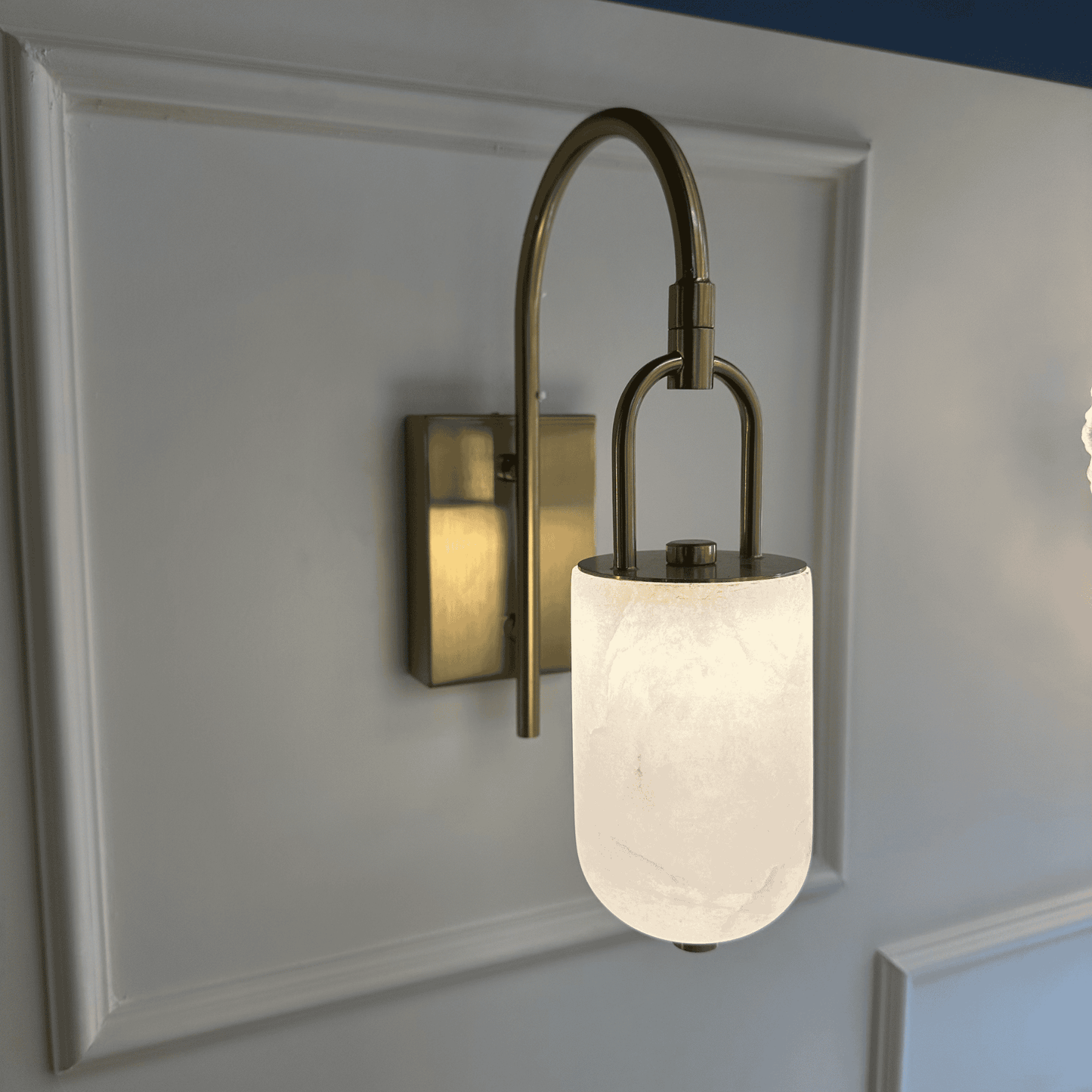 Modern brass and alabaster marble wall sconce with curved arm and soft lighting.