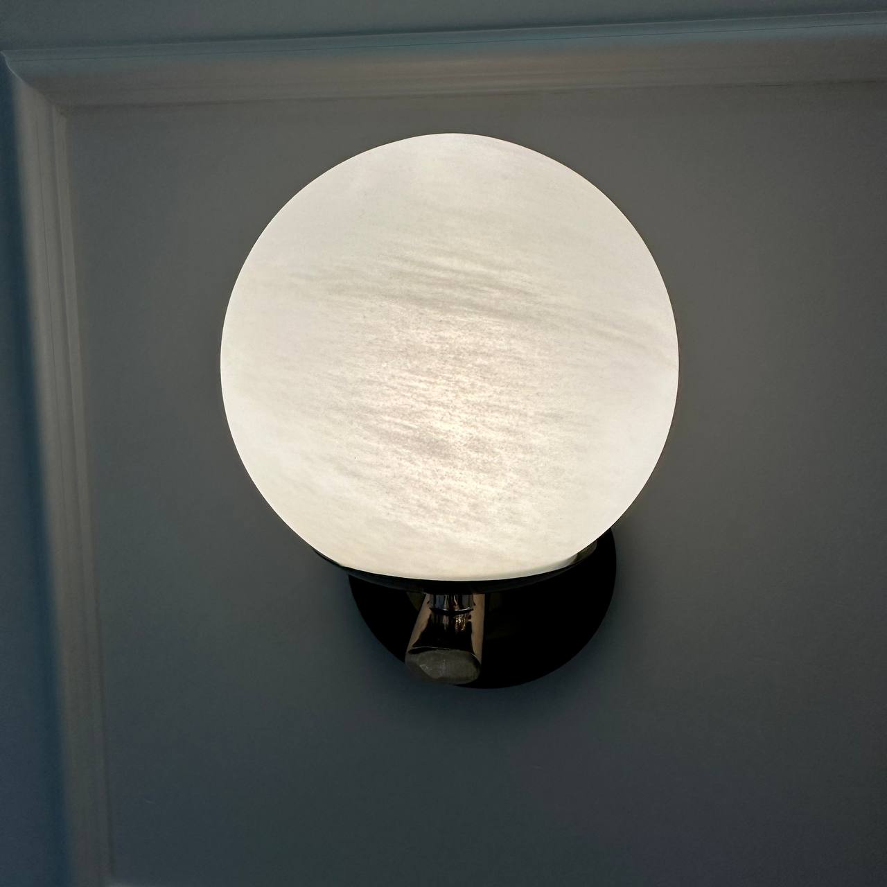 Front view of a glowing alabaster globe sconce mounted on a smooth white wall.