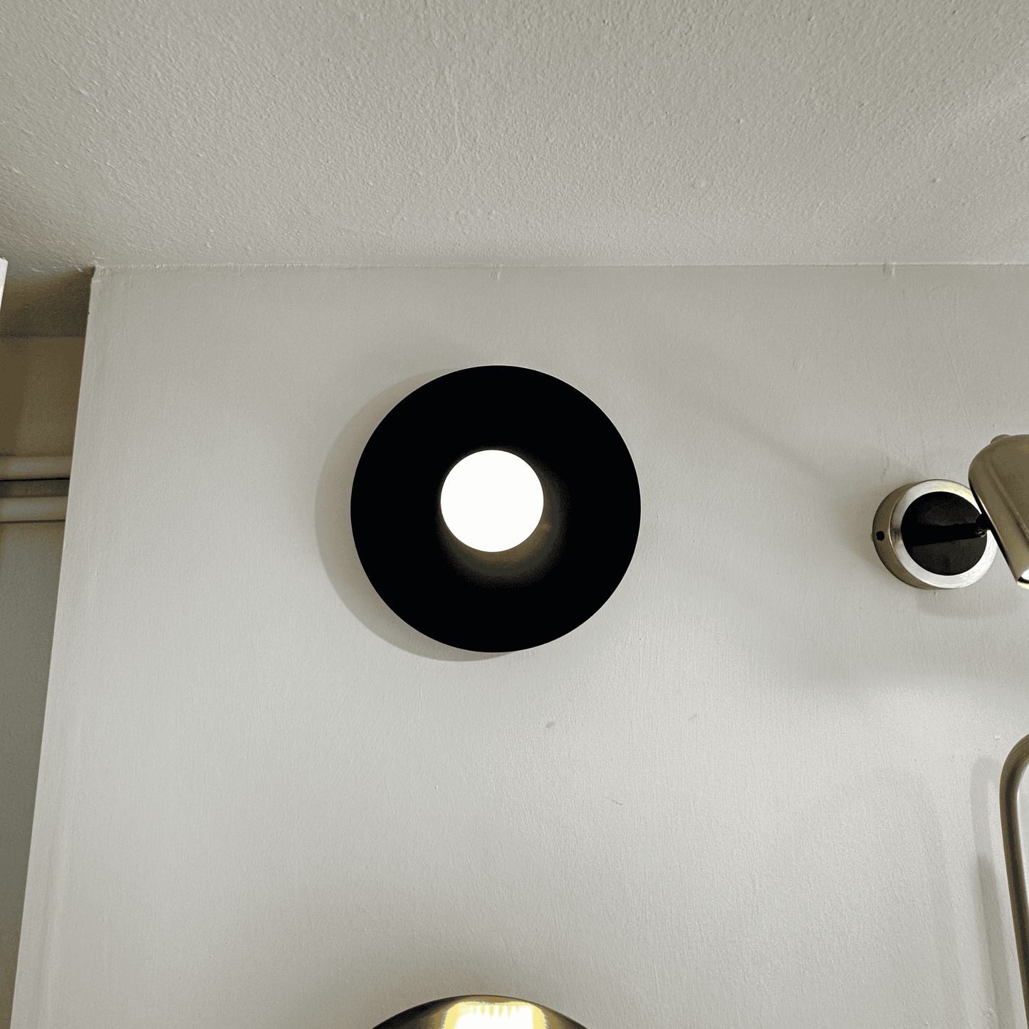 Angled view of black disc wall sconce casting ambient light against a clean white wall.