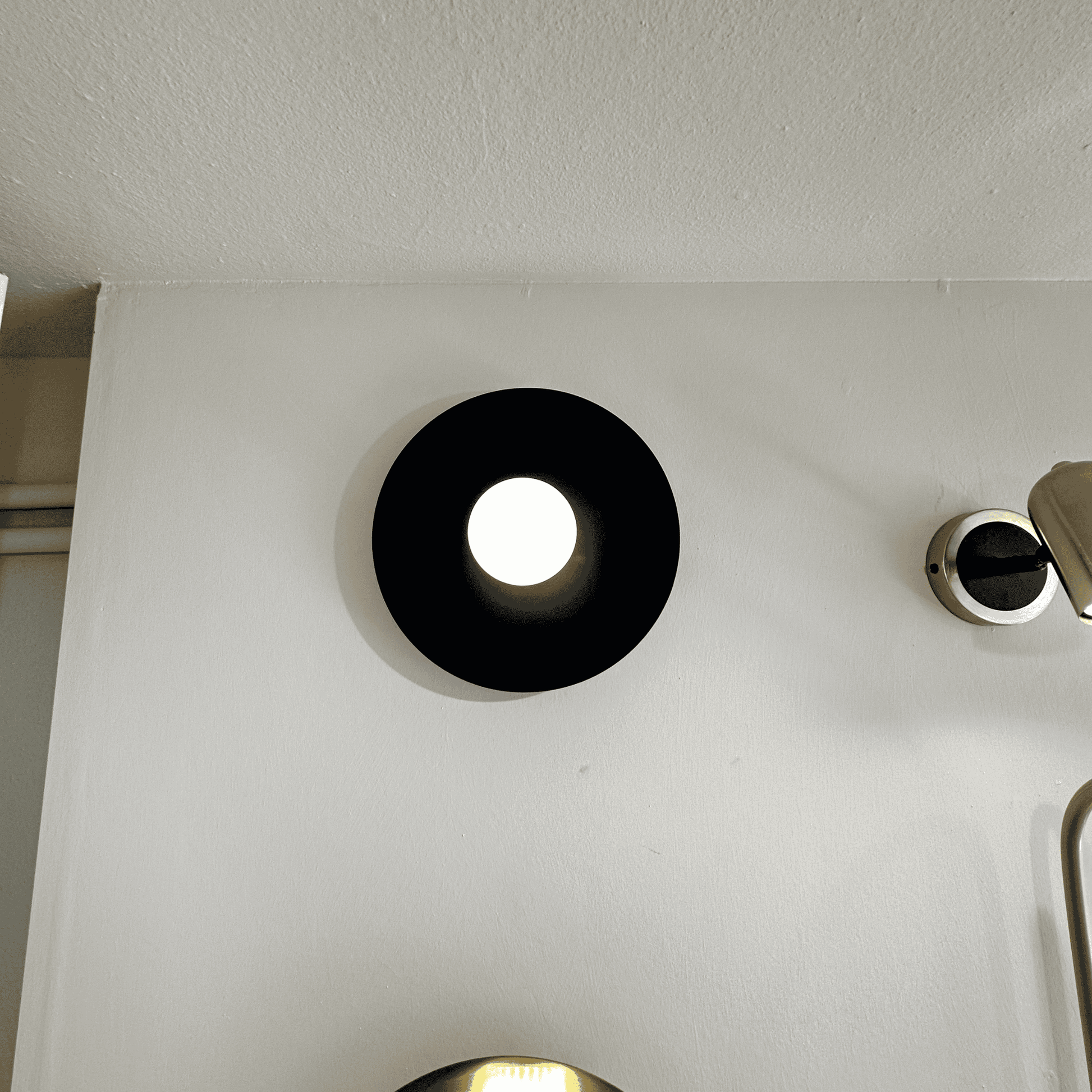 Angled view of black disc wall sconce casting ambient light against a clean white wall.