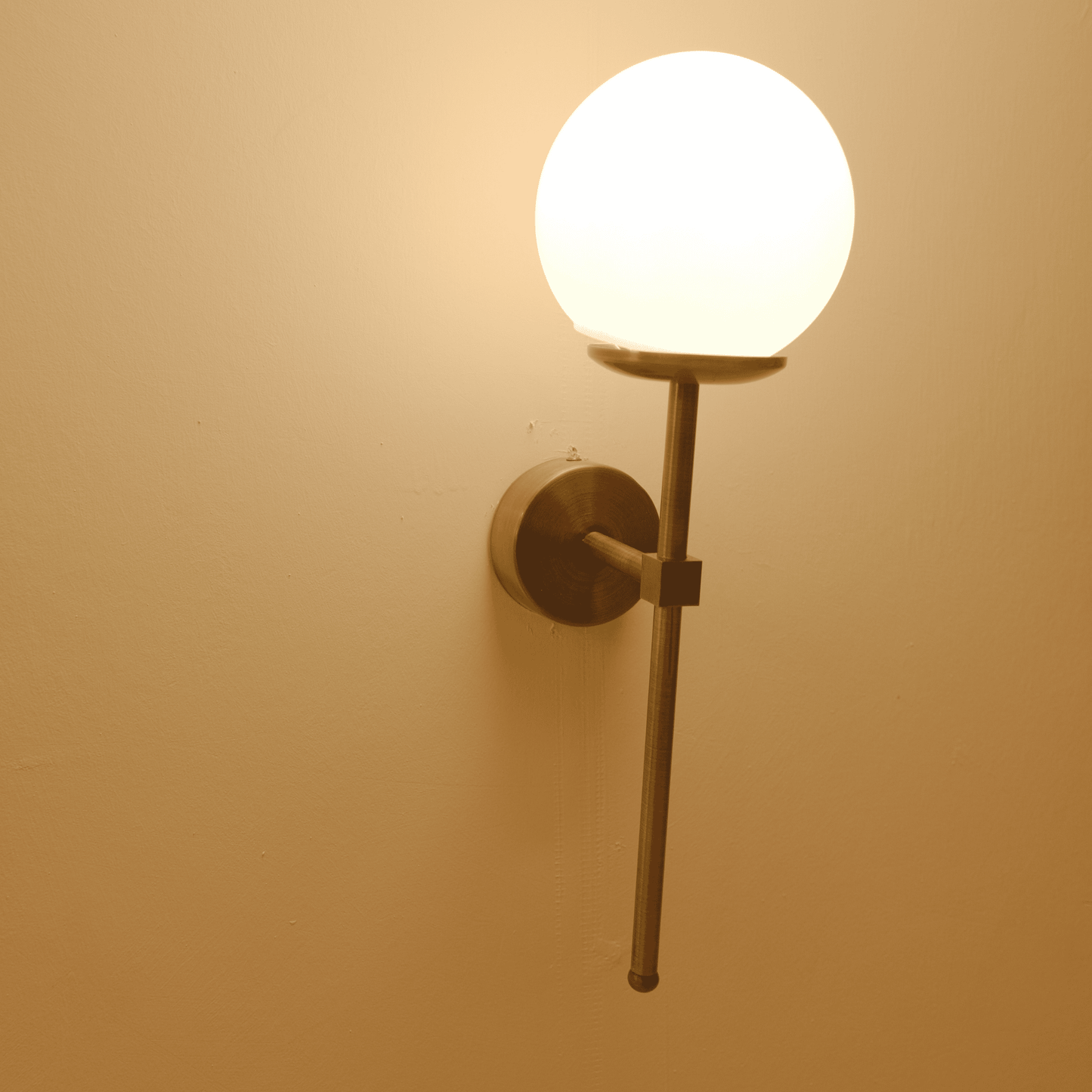 Angled view of a contemporary brass wall sconce with frosted globe shade on a neutral wall.
