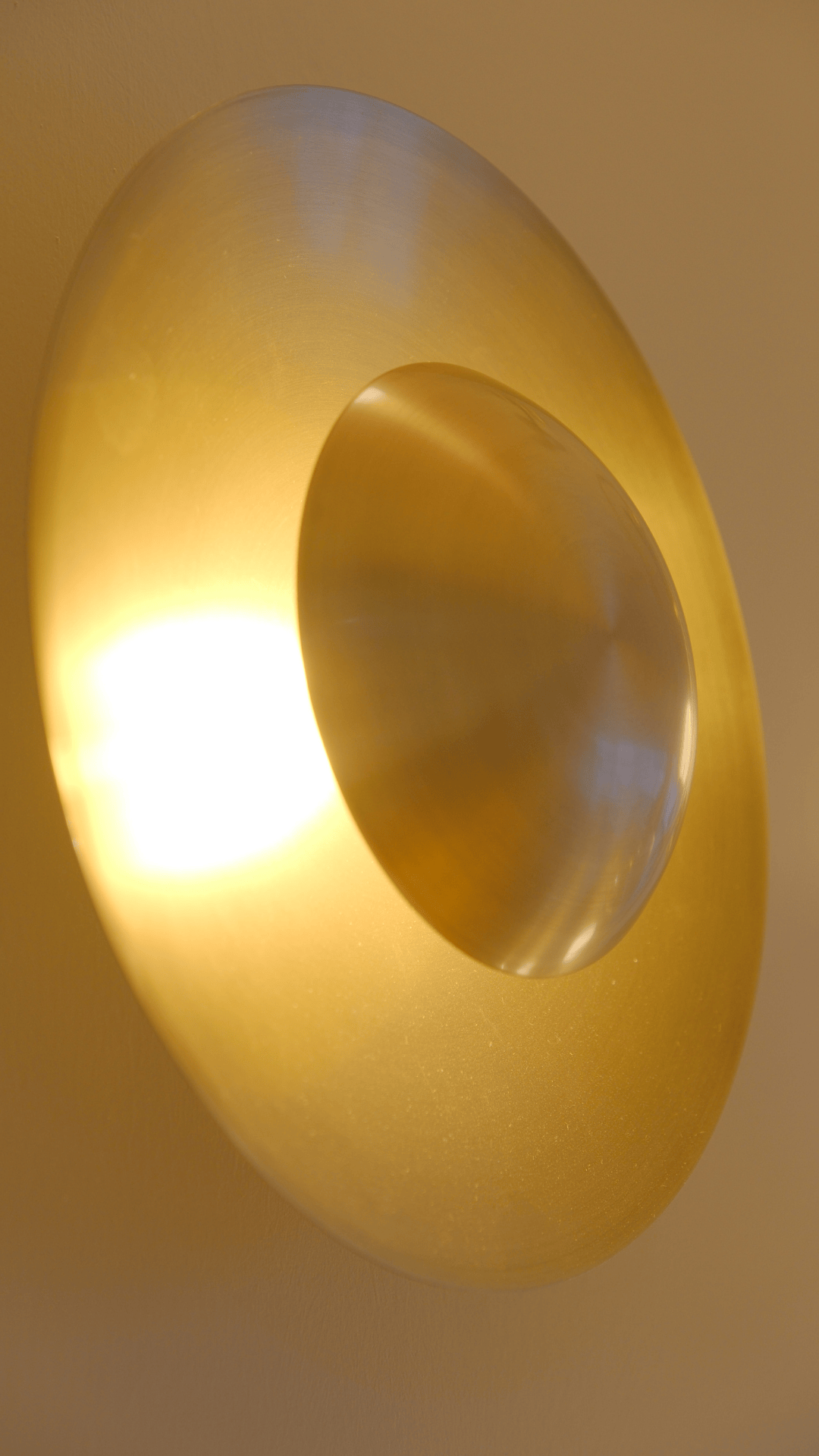 Angled brass wall sconce with radiant disk design providing modern ambient lighting.