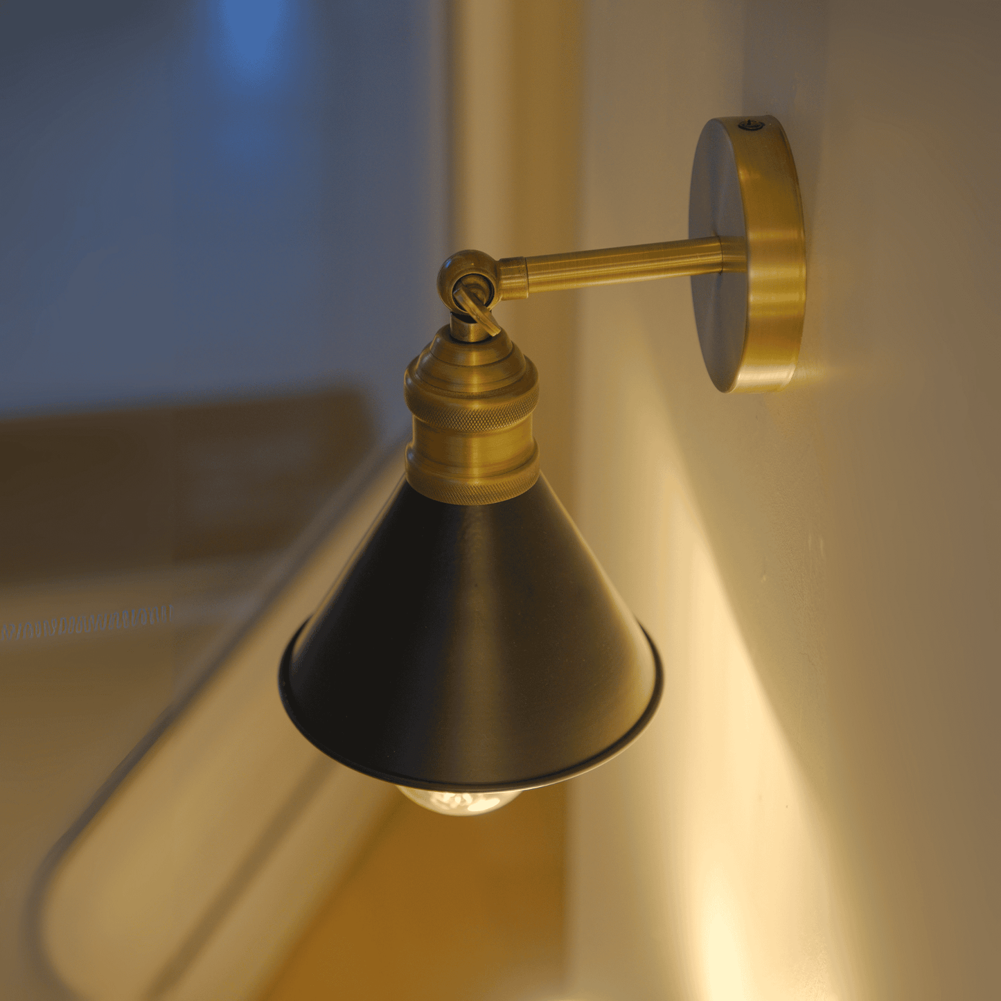 Angled night view of glowing wall sconce with black shade and brass hardware beside a window.