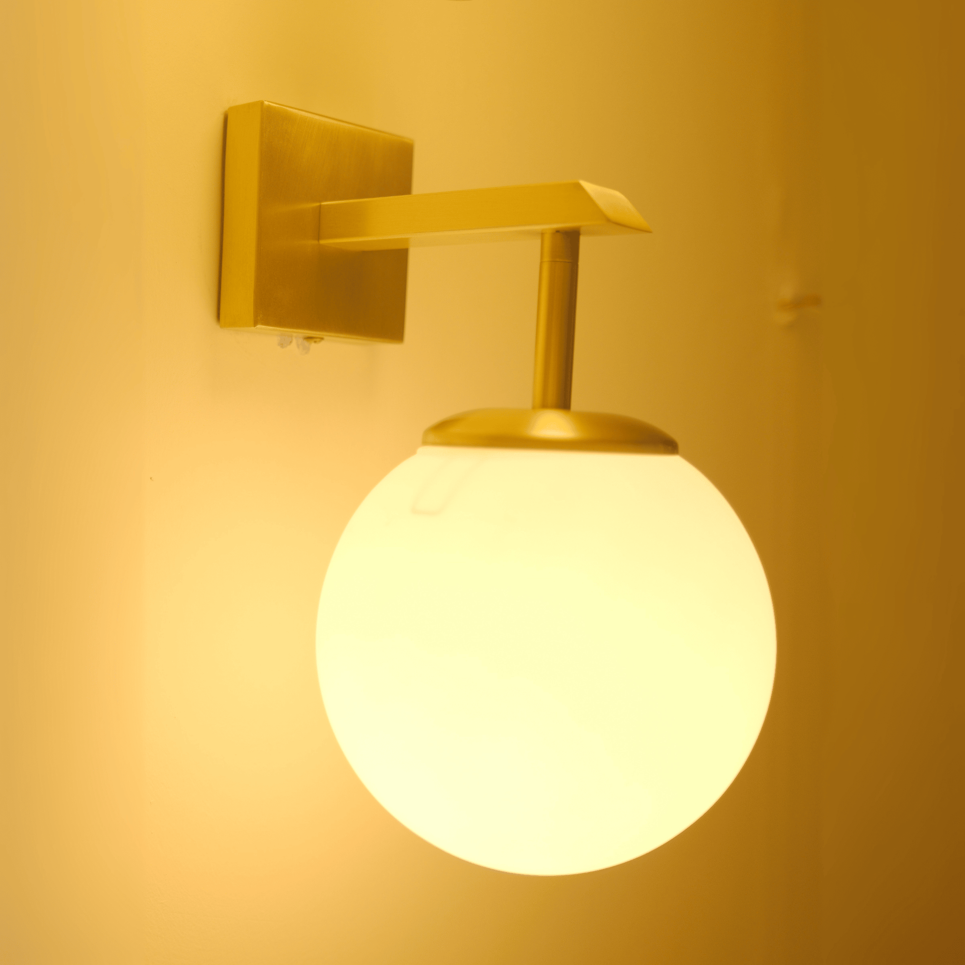 Angled view of a modern brass sconce with a matte opal globe providing soft accent lighting.