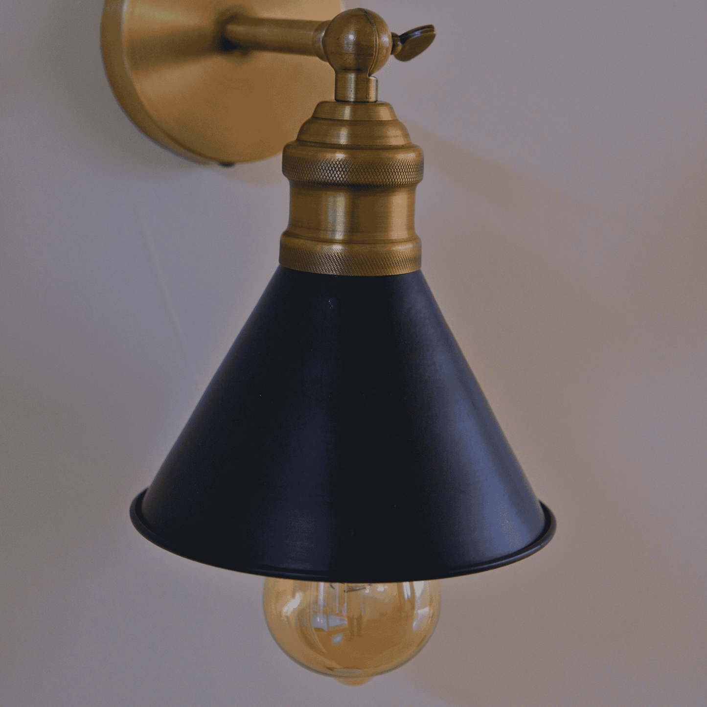 Side view of a black cone-shaped sconce with brass wall mount and visible bulb.