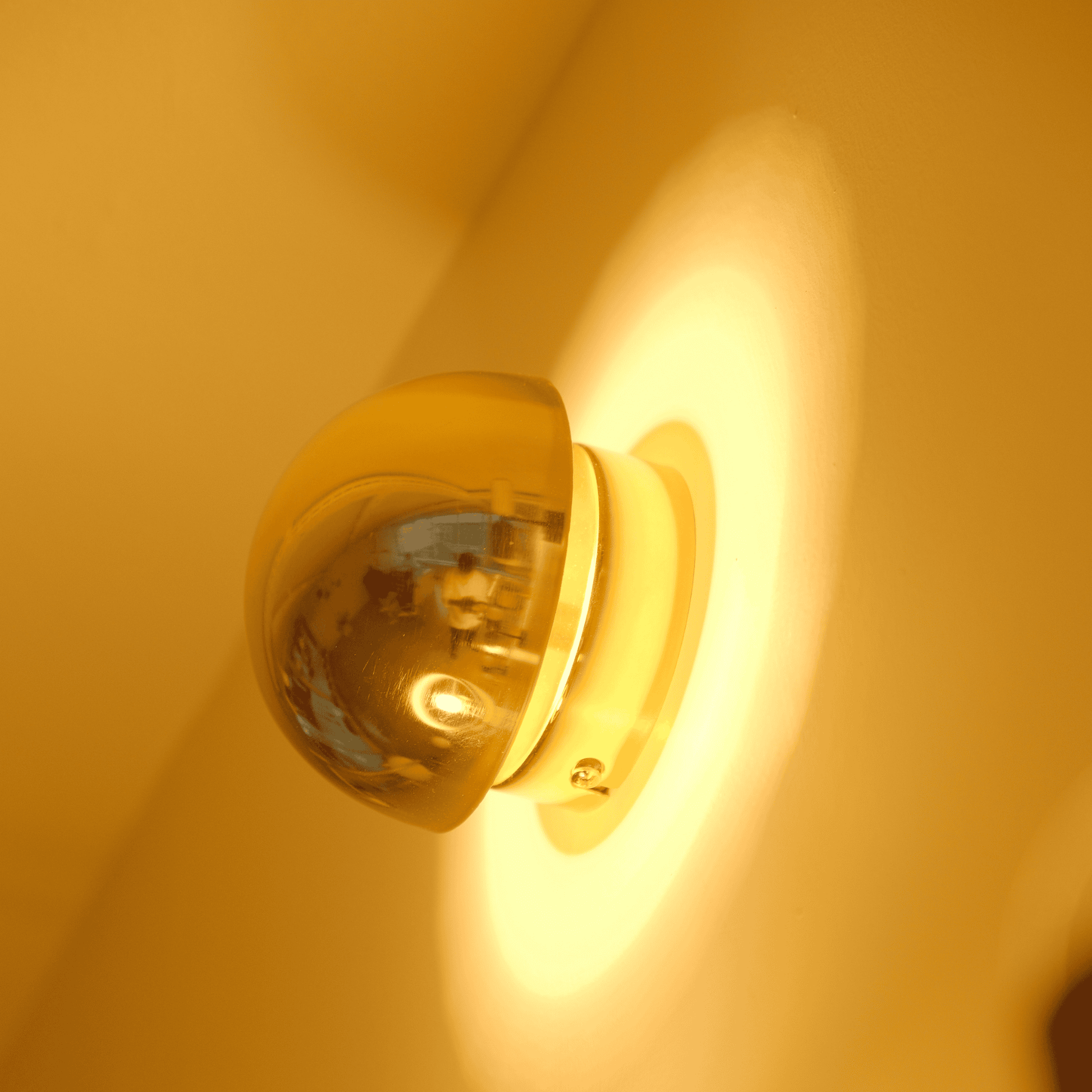 A brass sconce viewed from the side emits warm backlighting and highlights its smooth form.