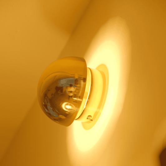 A brass sconce viewed from the side emits warm backlighting and highlights its smooth form.