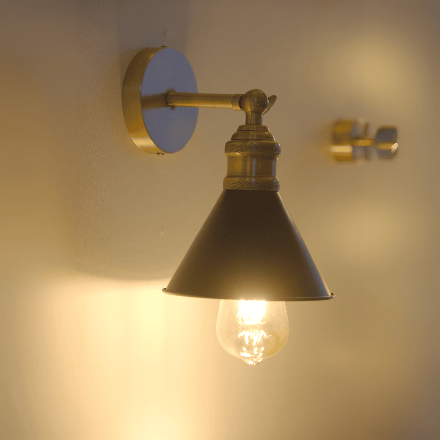 Side wall perspective of illuminated black and brass cone sconce.