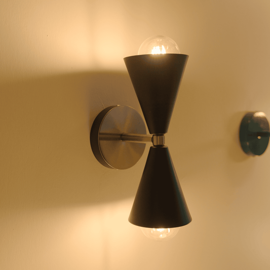 Illuminated black cone sconce with brass mount casting warm light on a beige wall.