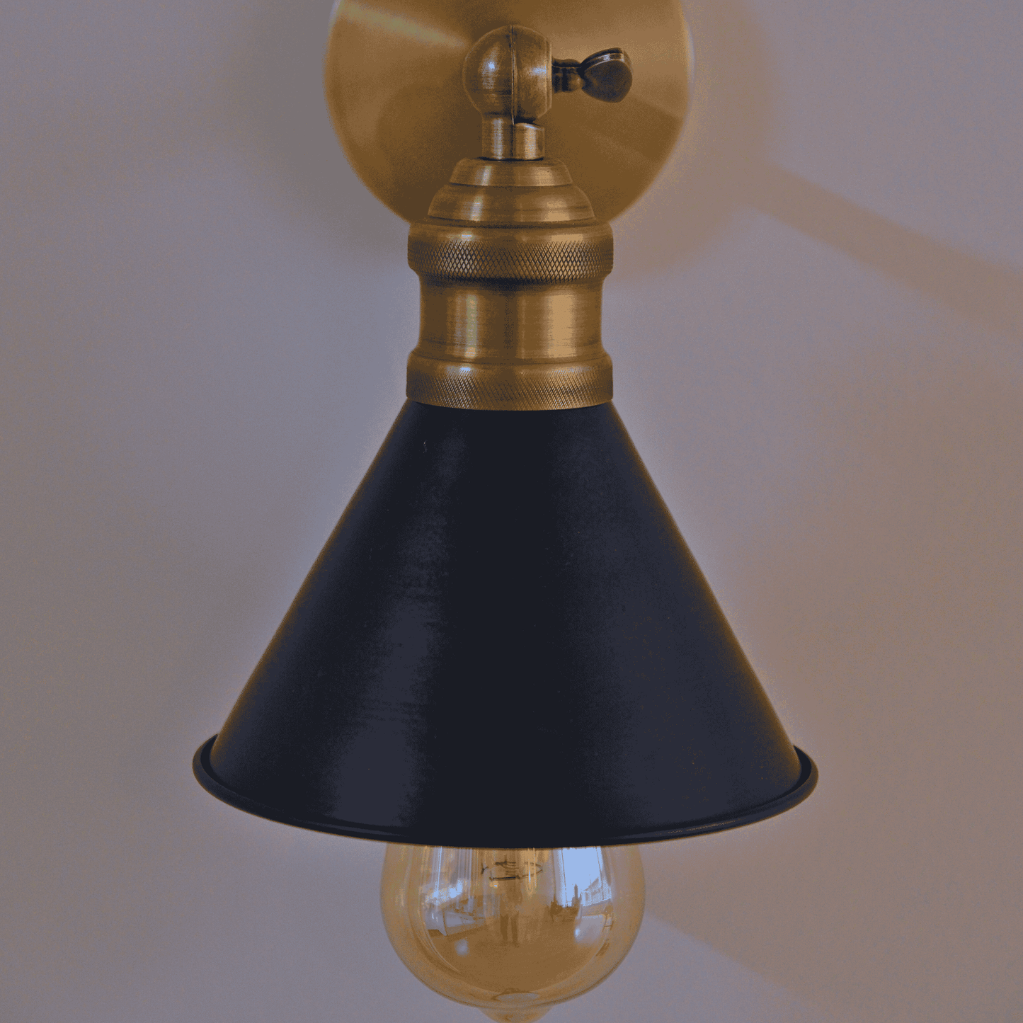 Black cone shade wall sconce with exposed bulb viewed from the front.