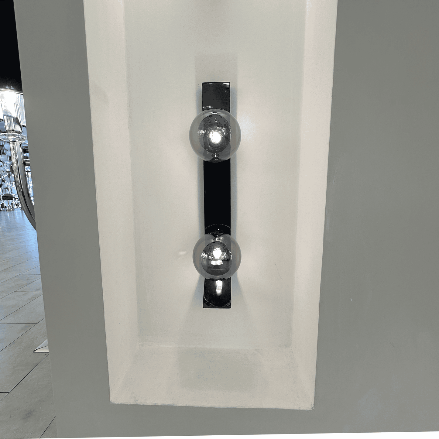 Black metal wall sconce with dual smoked glass globes recessed in a white wall niche.