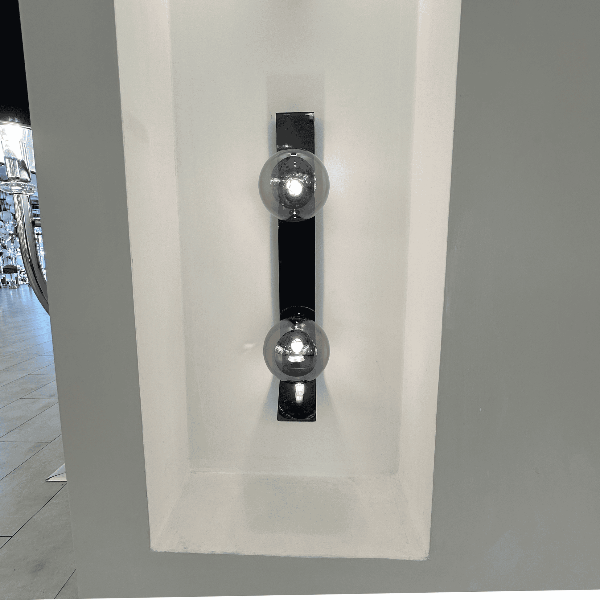 Black metal wall sconce with dual smoked glass globes recessed in a white wall niche.