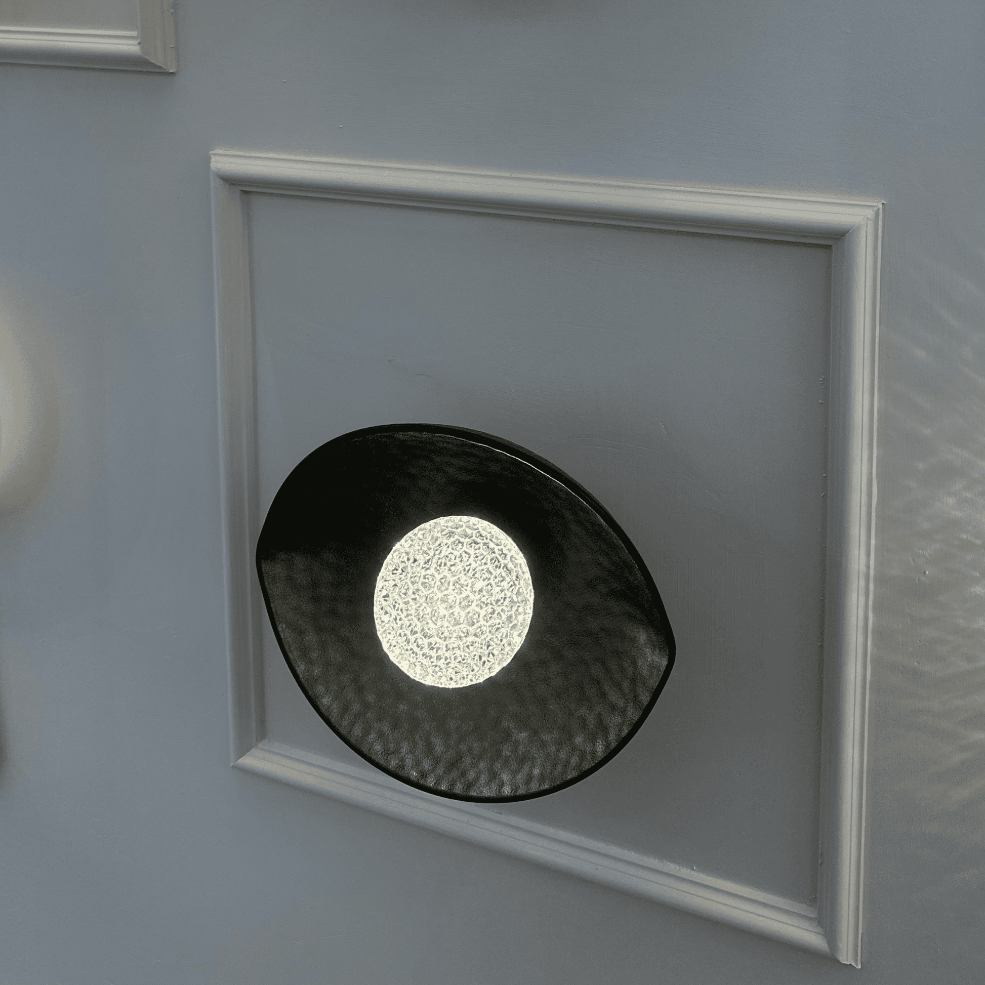 side view of a black plexiglass LED wall sconce with glowing textured diffuser and curved shape.