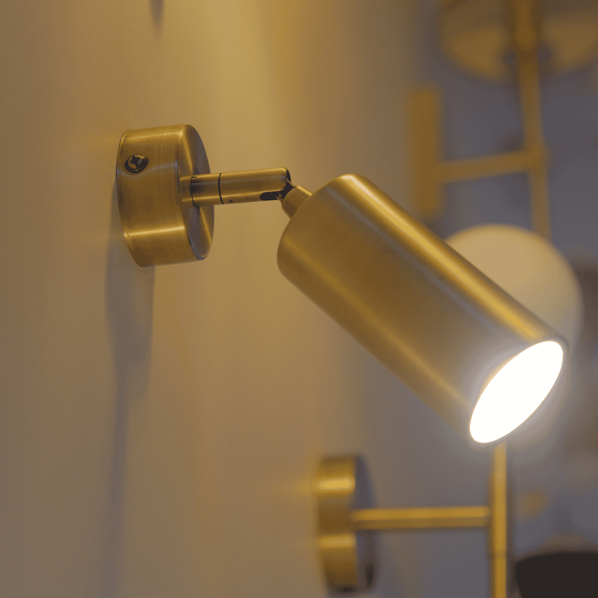 Adjustable brass wall sconce with cylindrical form mounted on wall for focused lighting.