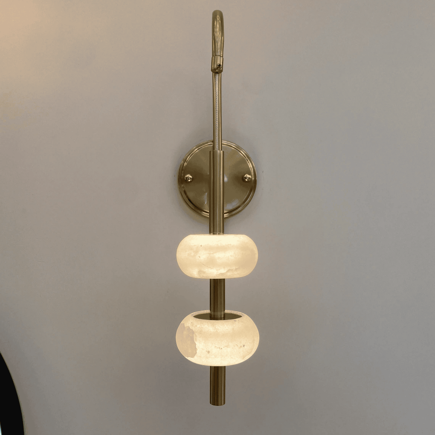 Wall-mounted brass sconce with dual alabaster diffusers in a minimalist lighting design.