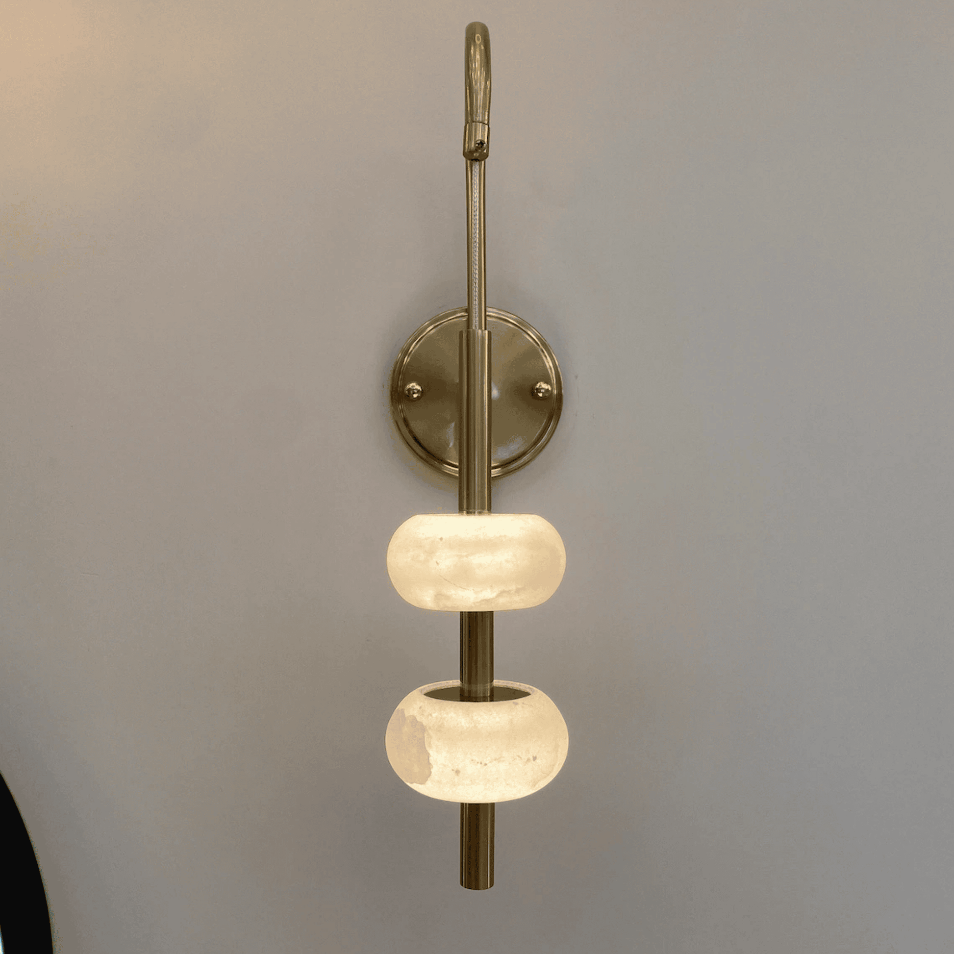 Wall-mounted brass sconce with dual alabaster diffusers in a minimalist lighting design.