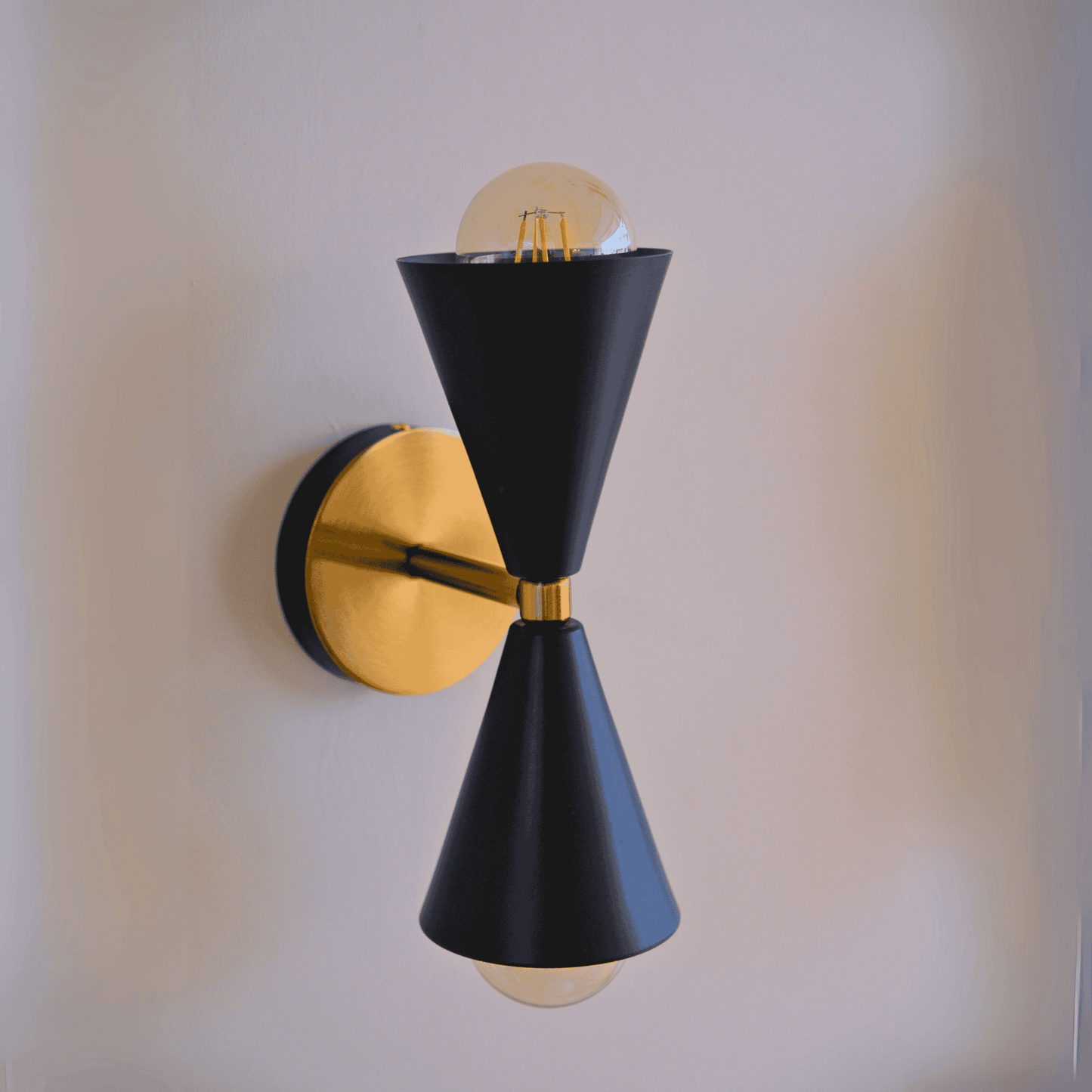 Matte black double cone sconce with brass backplate mounted on an interior wall for a modern lighting effect.