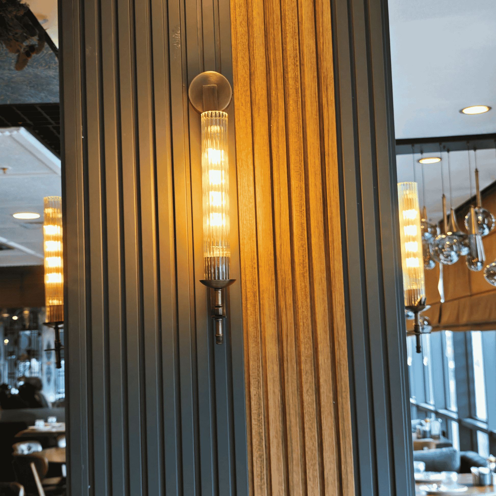 Ribbed vertical wall sconce mounted at a corner between brass and mirror elements