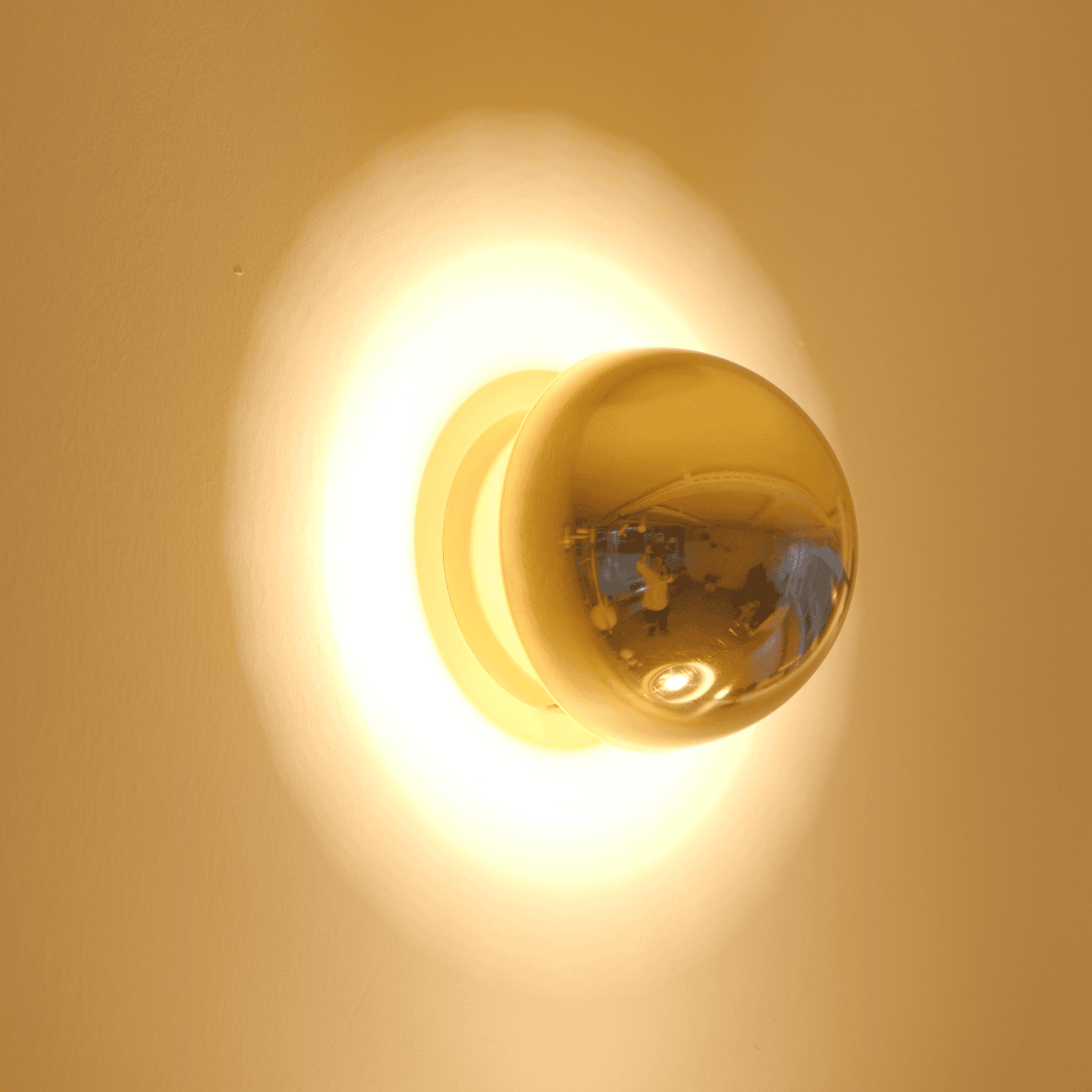 A brass globe wall sconce provides warm illumination against a neutral wall for a modern aesthetic.