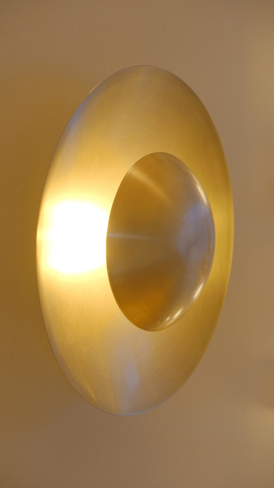 Brass halo wall sconce with convex center and warm ambient illumination.