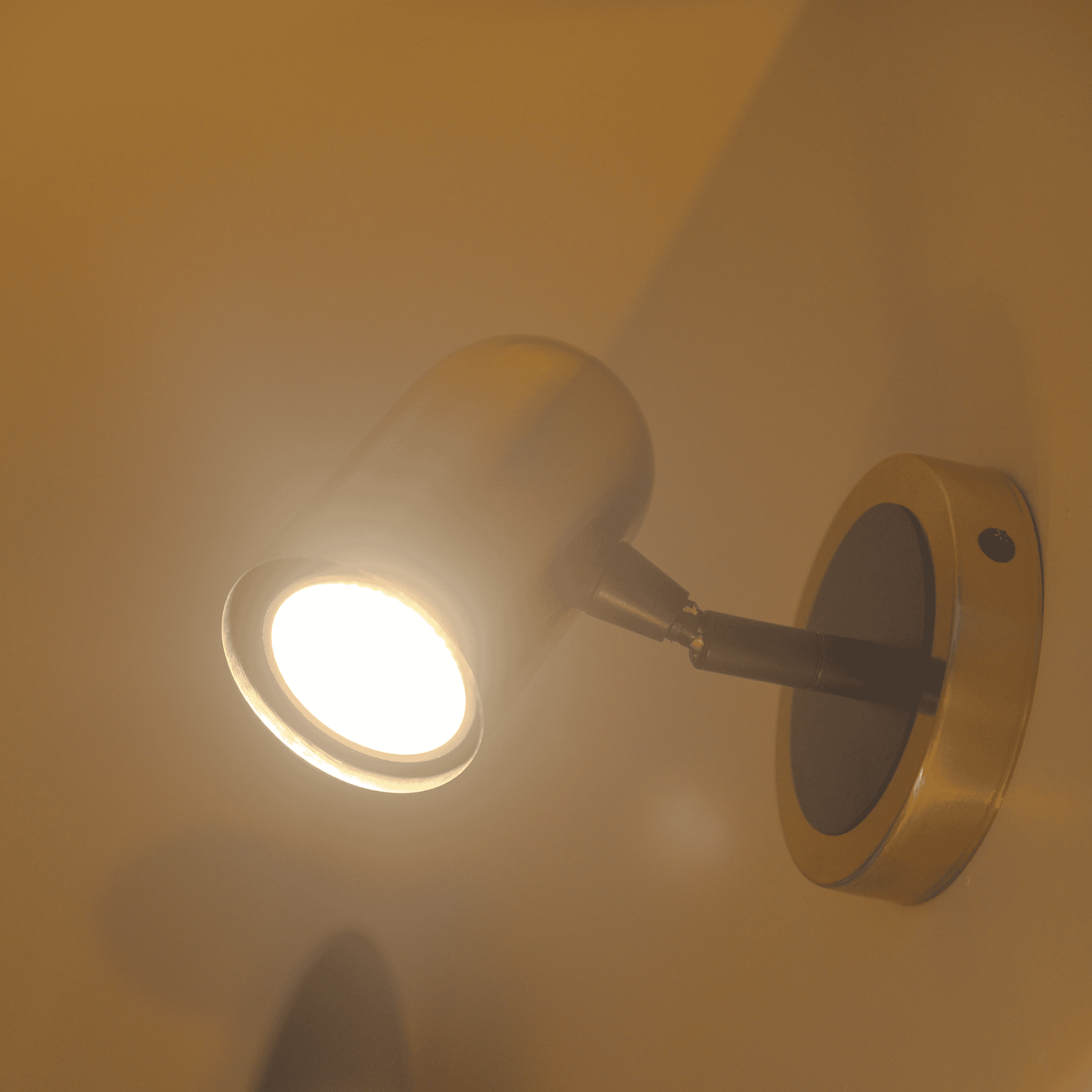 Directional brass wall sconce with focused LED lighting on a neutral wall.