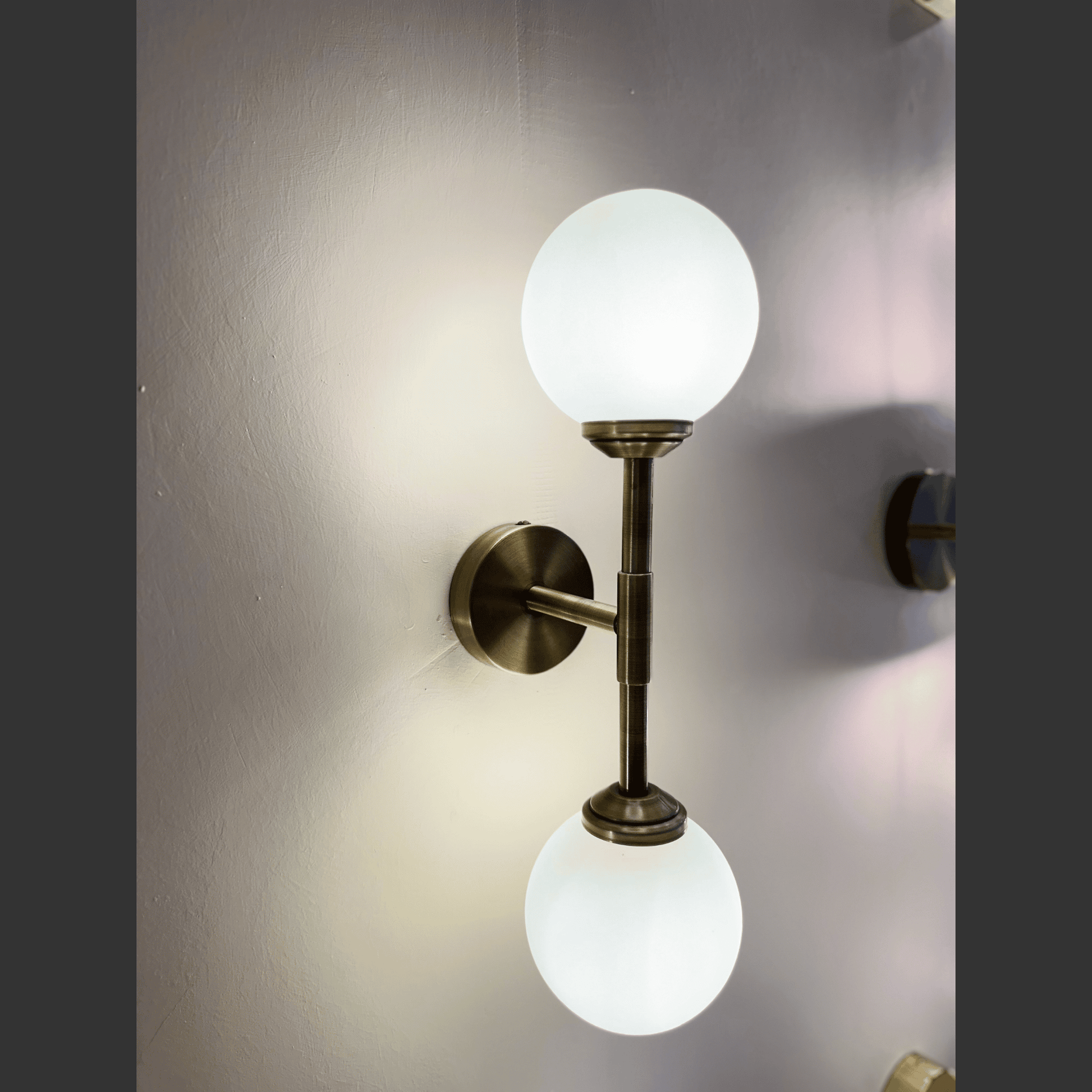 Wall-mounted light fixture with two glass globe lights on a neutral wall.