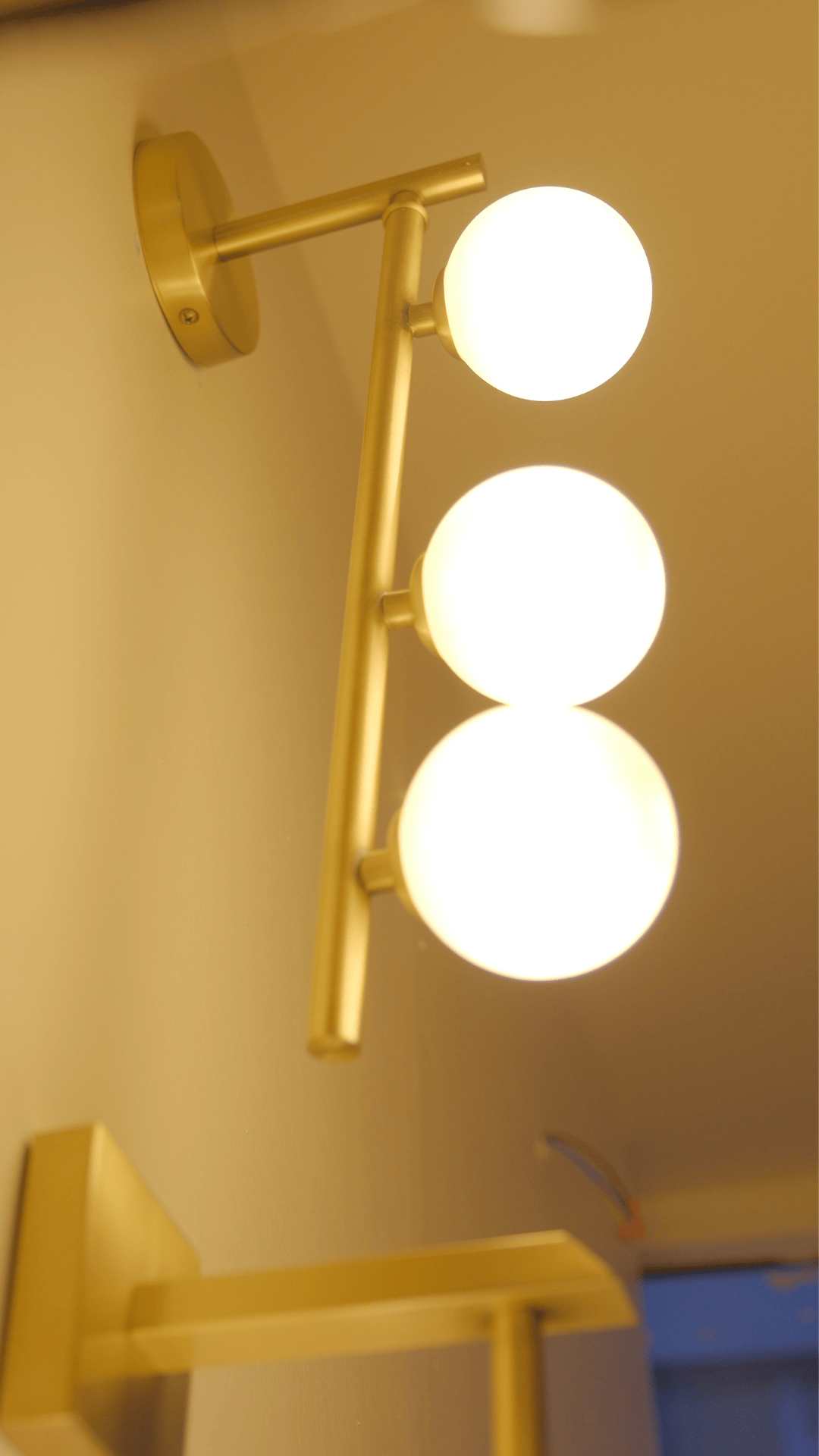 Upward angle of brass wall fixture with three glowing opal globes for soft ambient lighting.