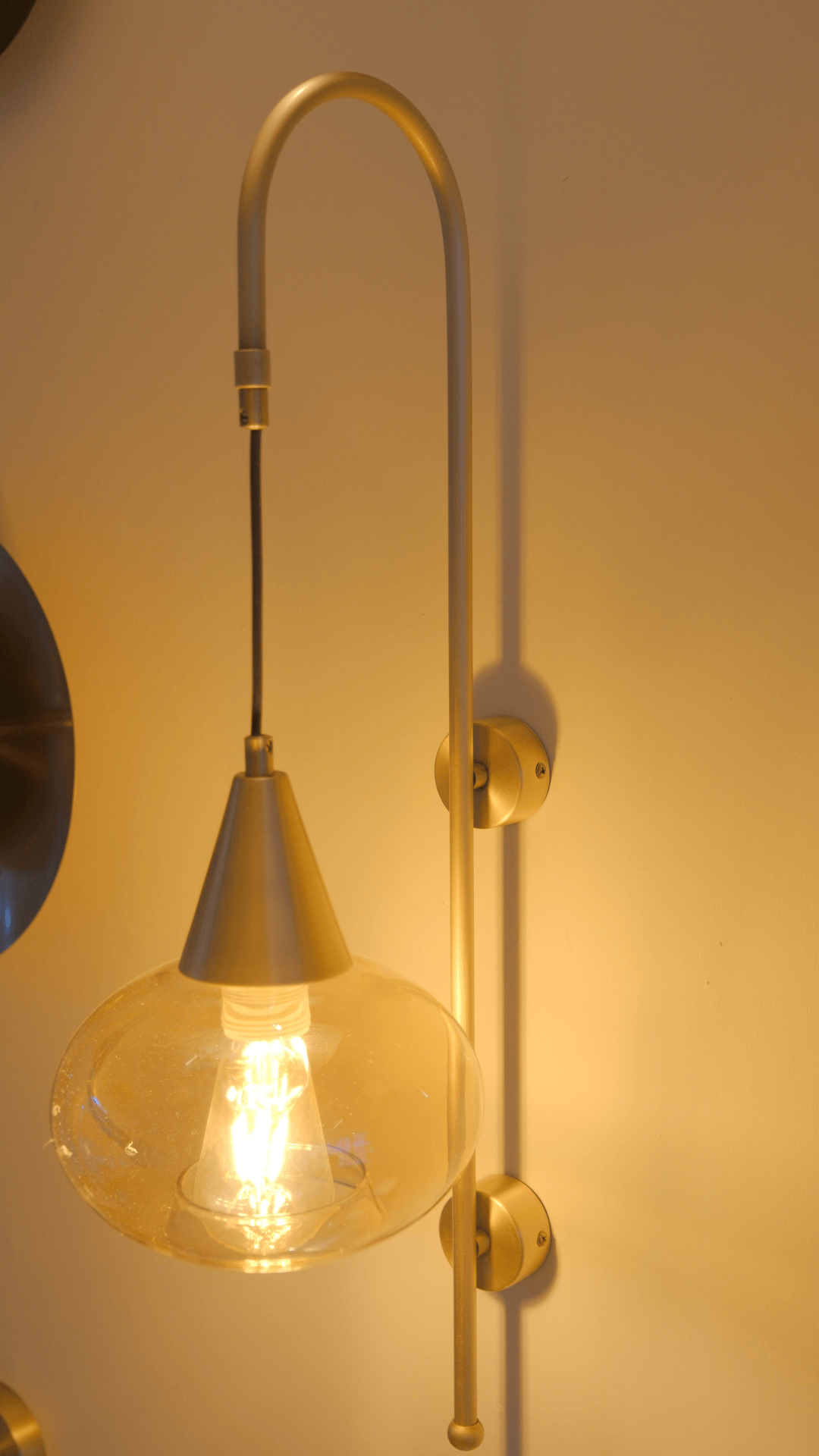 Elegant brass wall light with suspended clear globe shade mounted on interior wall.