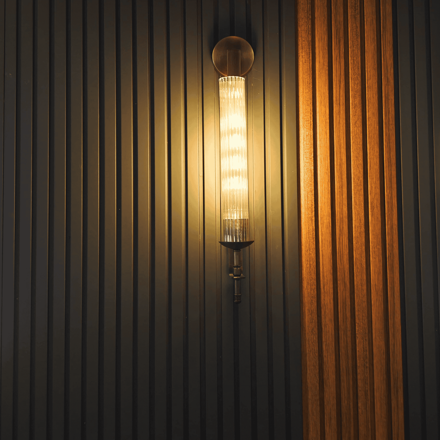 Antique brass wall sconce with fluted glass, mounted on a textured wood panel wall