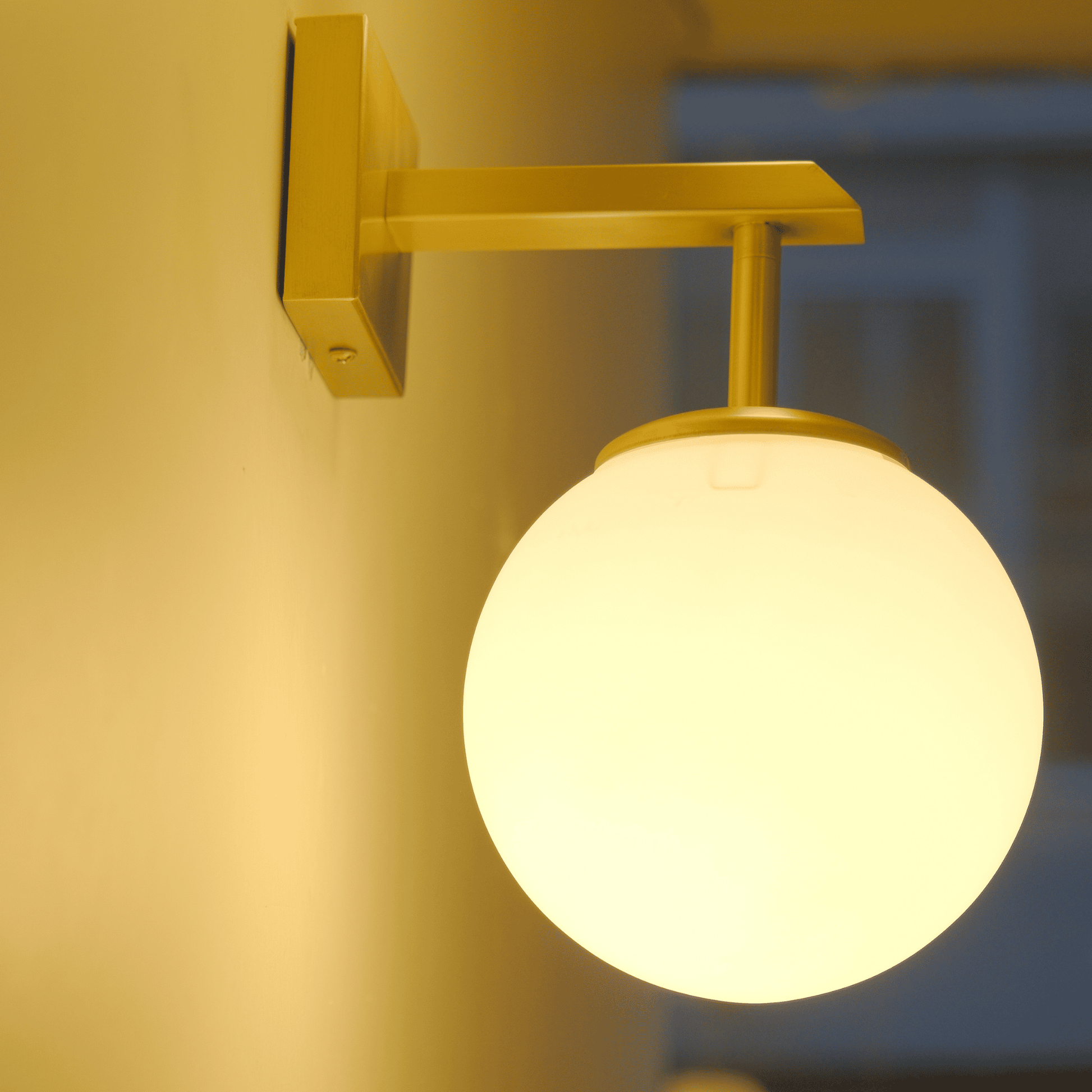 Brass wall sconce with glowing opal globe captured in dim lighting at dusk.