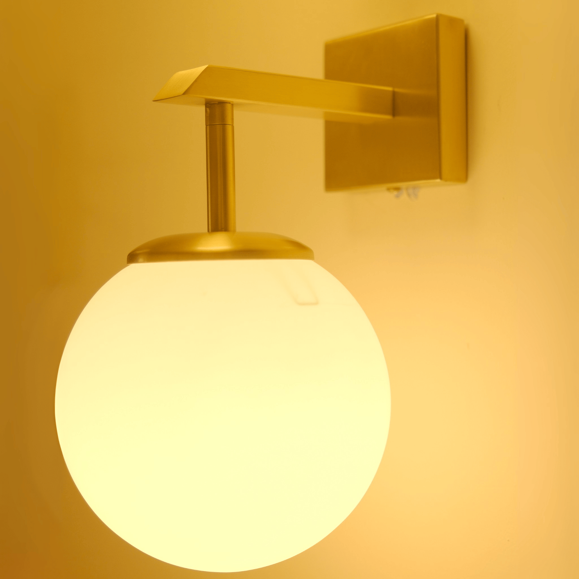 Side view of brass wall sconce with frosted globe shade for soft diffused lighting.