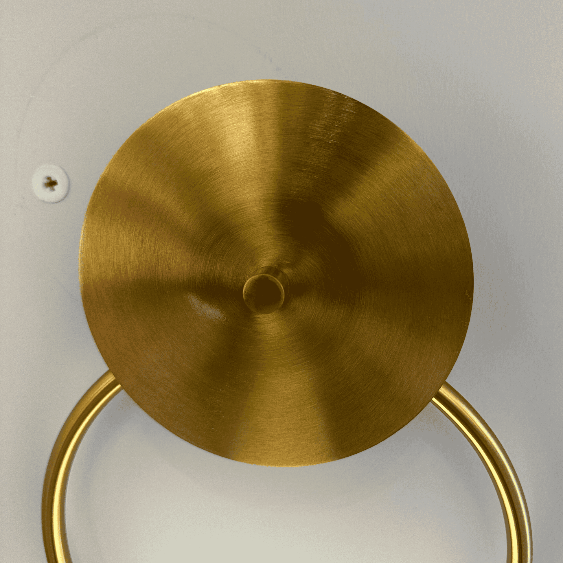 Close-up image showing round brass wall sconce mounting plate and curved arm attachment