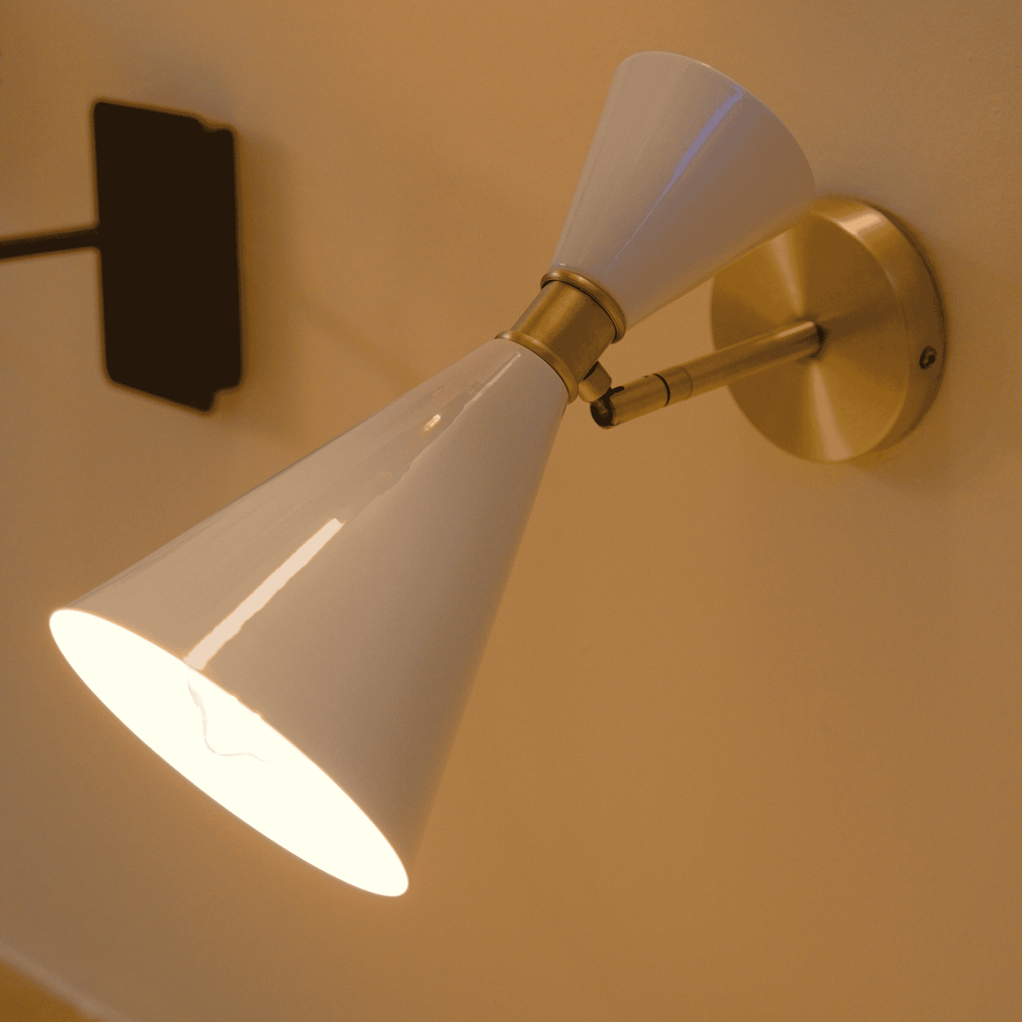 Brass and white wall sconce with adjustable arm and double-cone design for focused directional lighting.