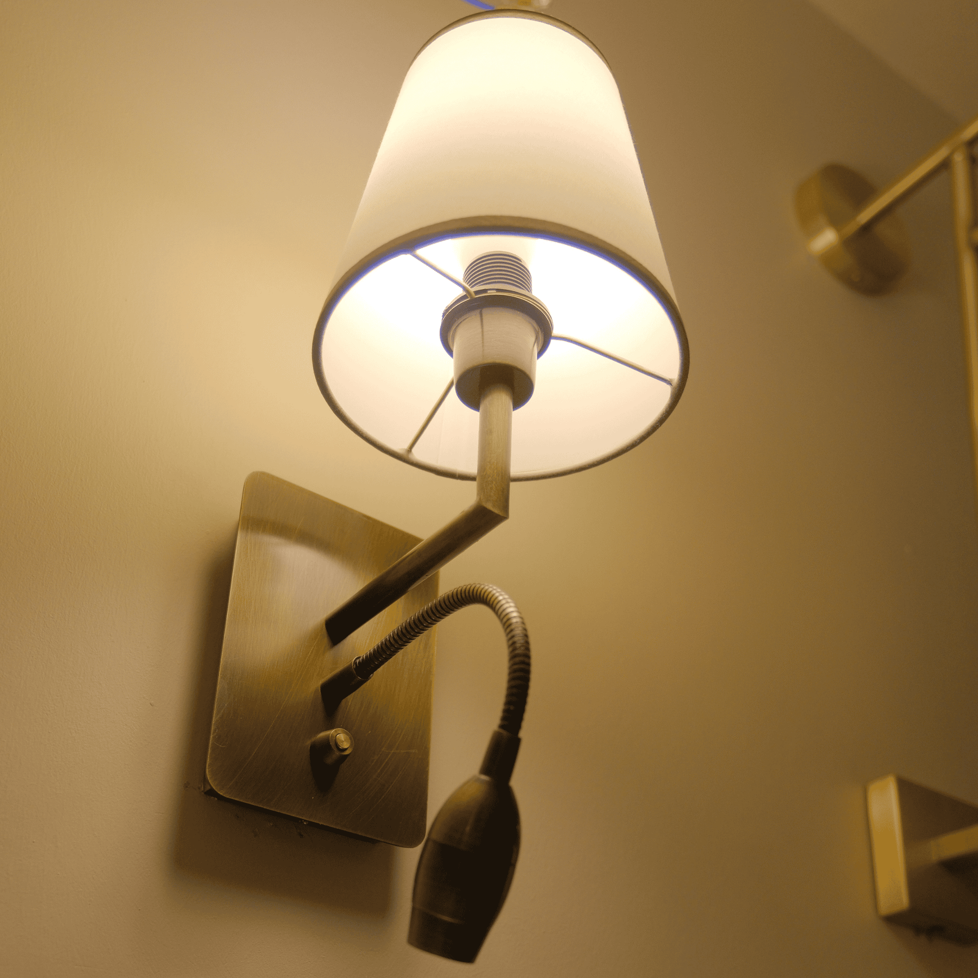 Brass wall sconce with fabric shade and built-in LED gooseneck light.