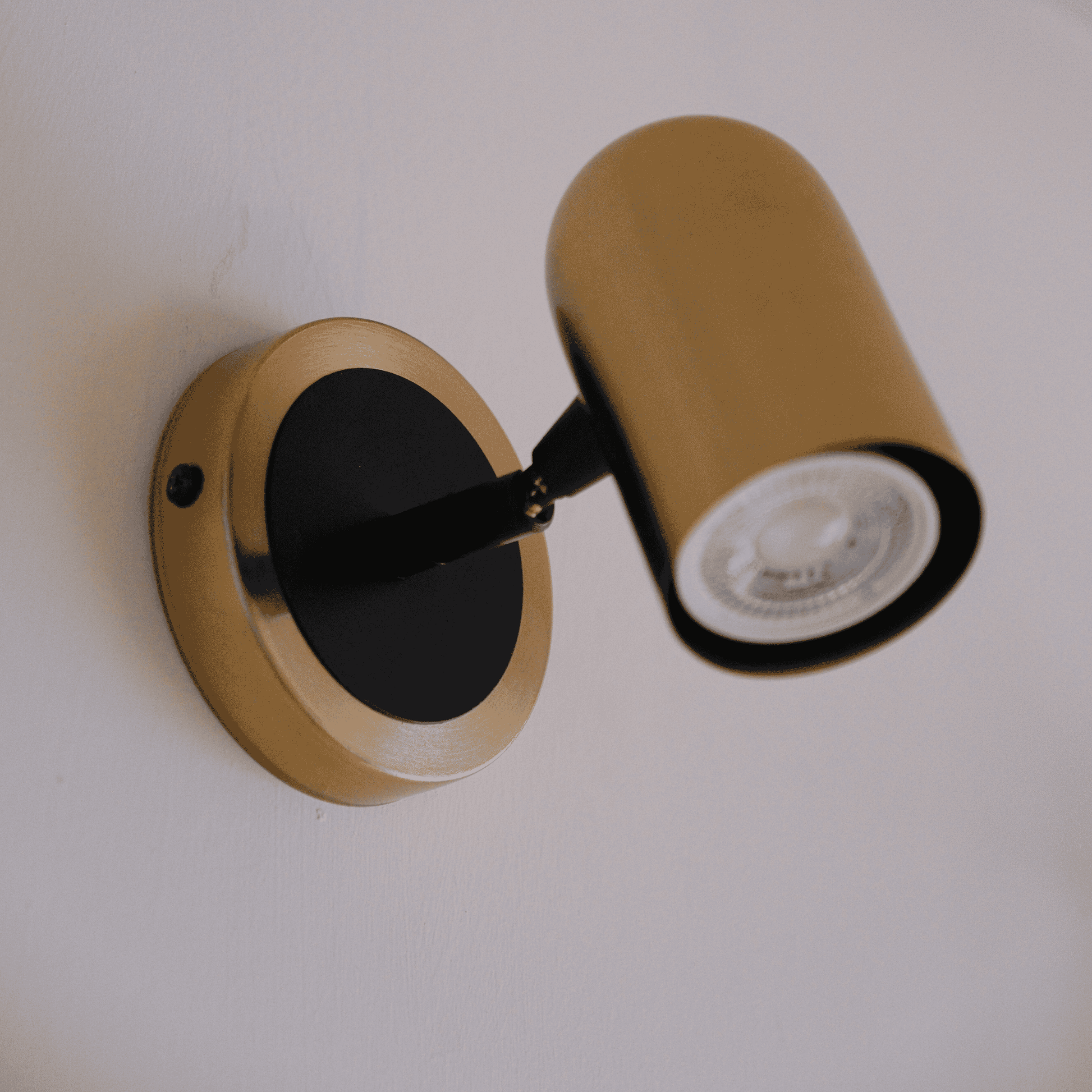 Brass wall spotlight with visible LED bulb and black base on a white wall.