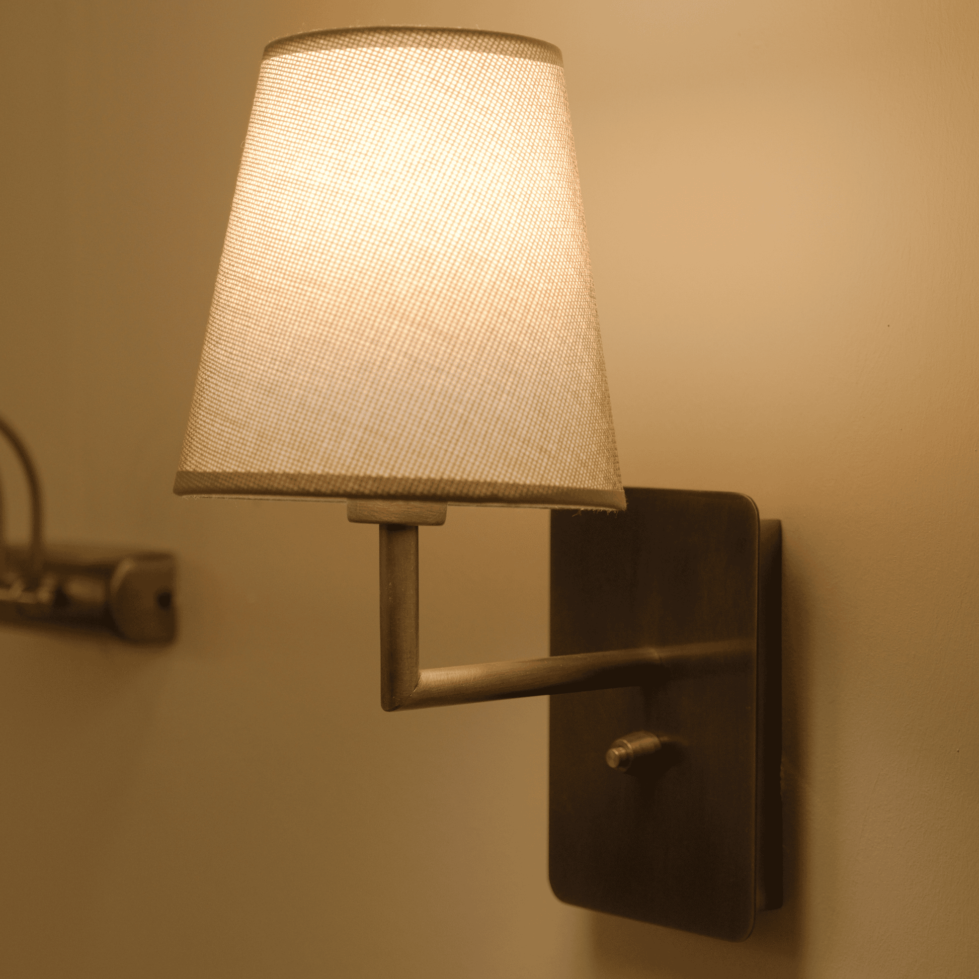 Bronze wall-mounted sconce with a softly glowing fabric shade for modern indoor lighting.