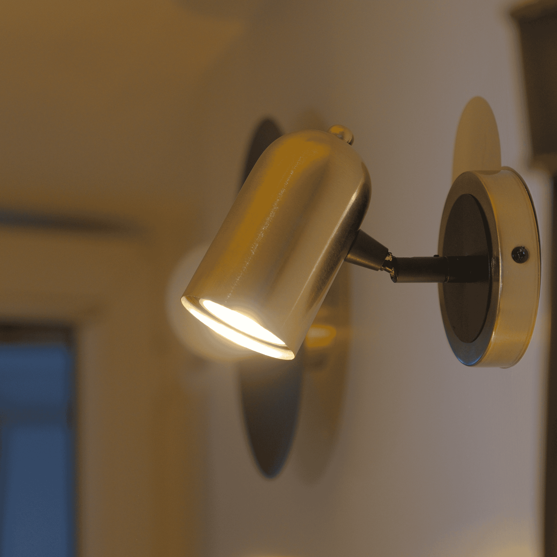 Brushed brass wall sconce with cylindrical head in a modern hallway.