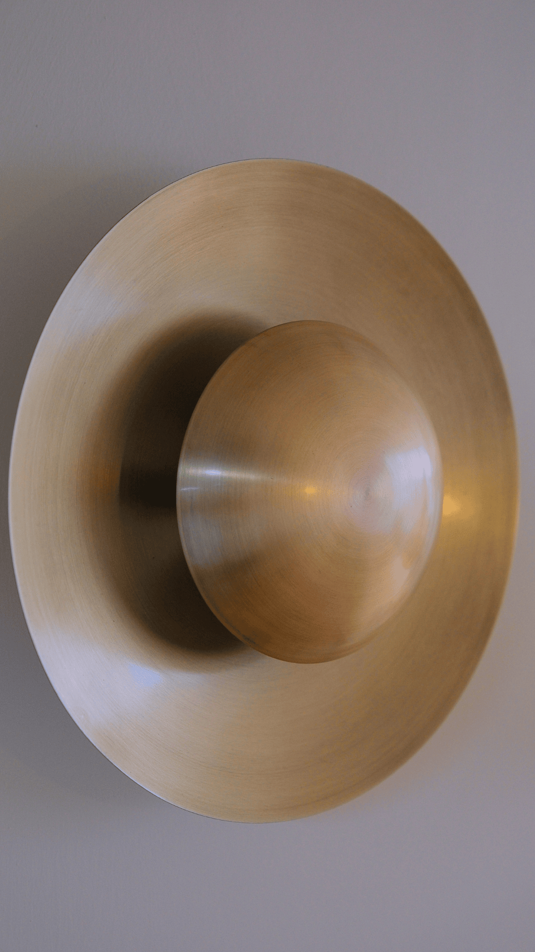 Brushed brass wall sconce with domed center and circular backplate ideal for modern interior lighting.