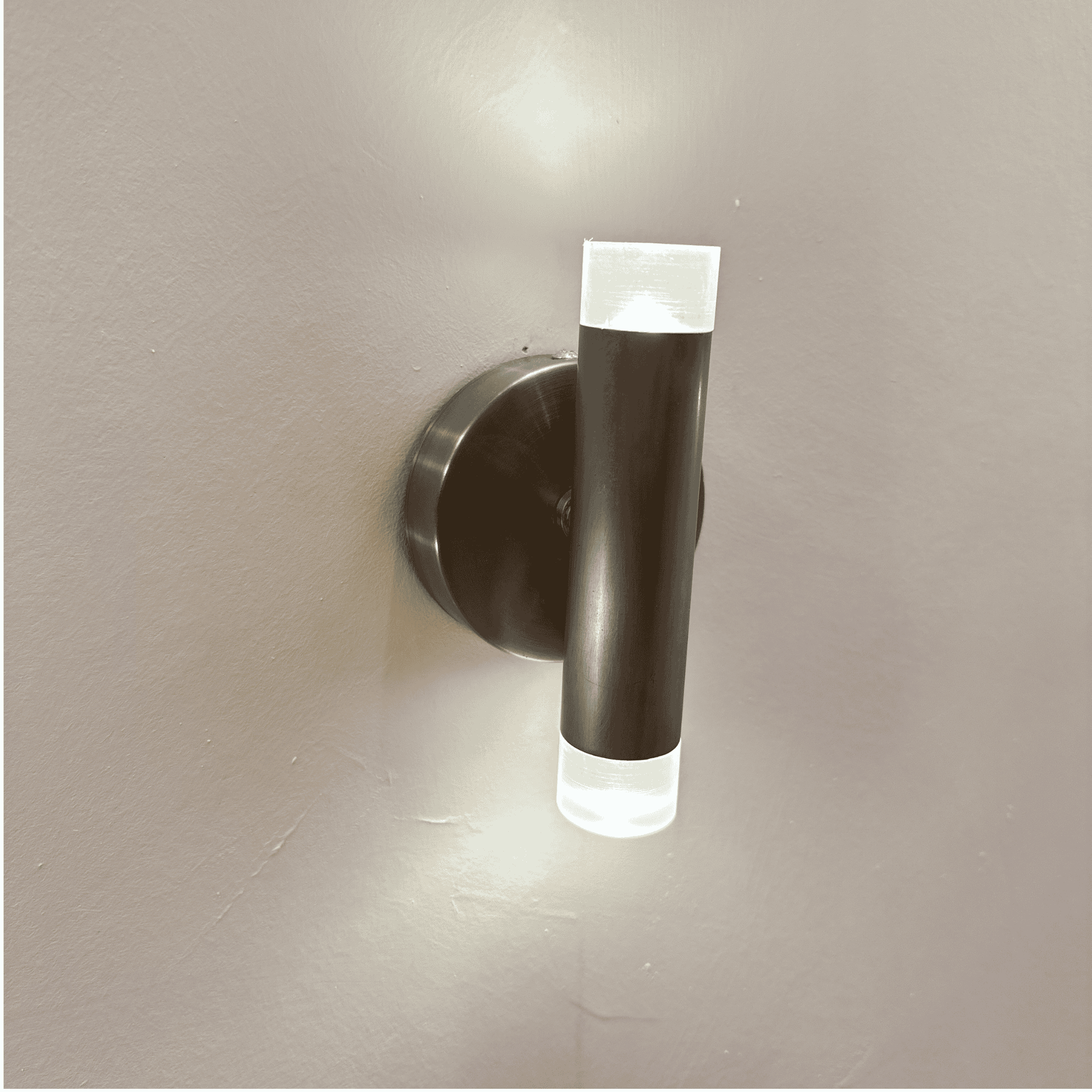 Brushed metal cylindrical LED wall sconce with upward and downward light diffusion mounted on an interior wall.
