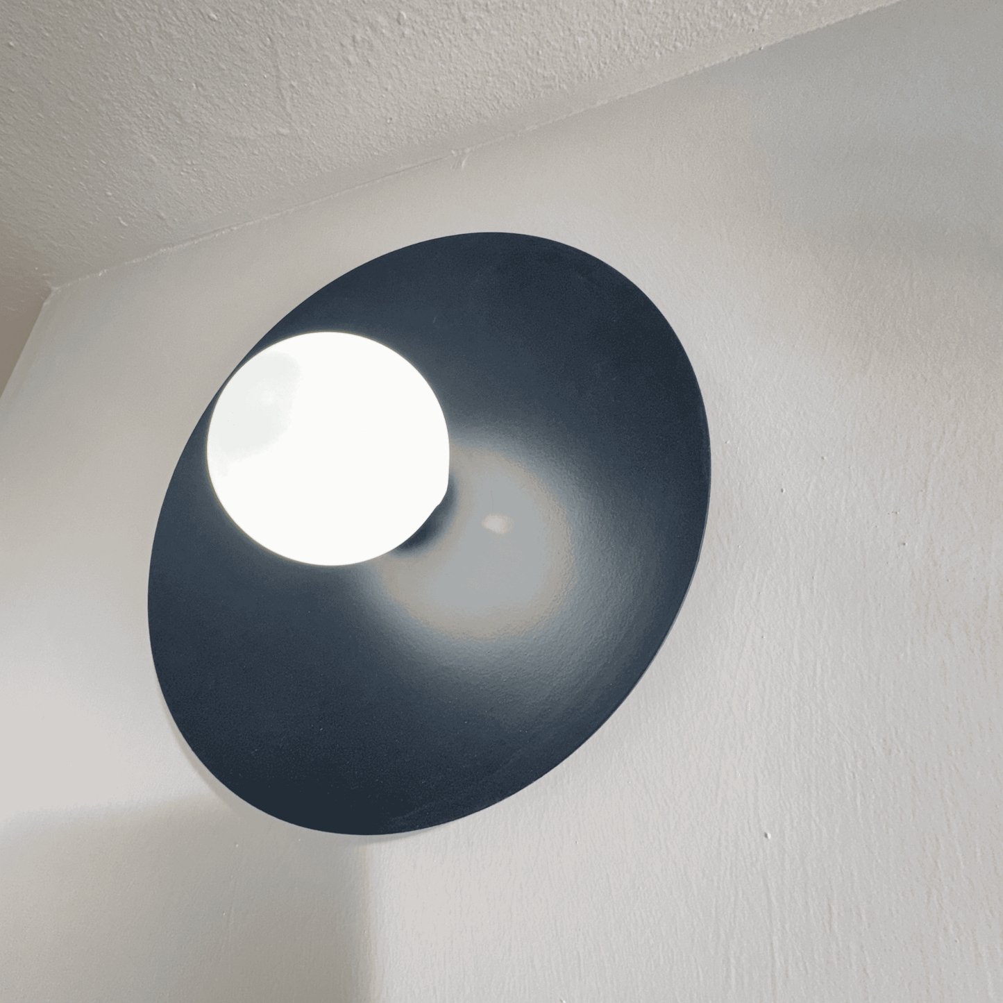 Centered black disc wall sconce emitting soft white light on a minimalist wall surface.