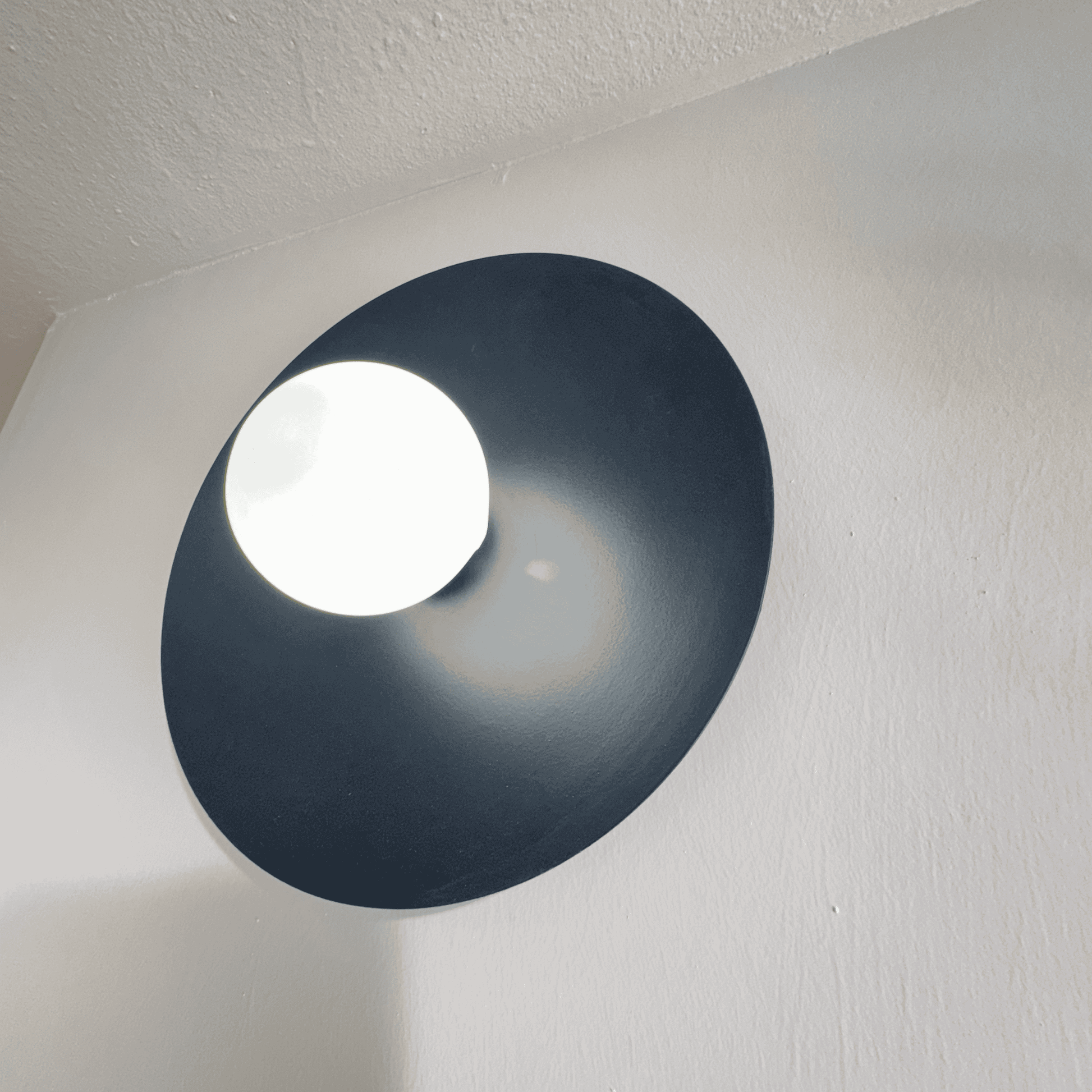 Centered black disc wall sconce emitting soft white light on a minimalist wall surface.