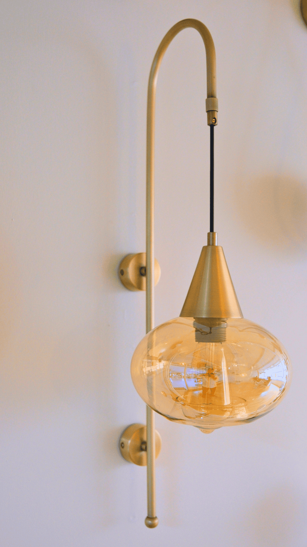 Modern brass wall sconce with amber-toned clear glass shade on vertical mount.