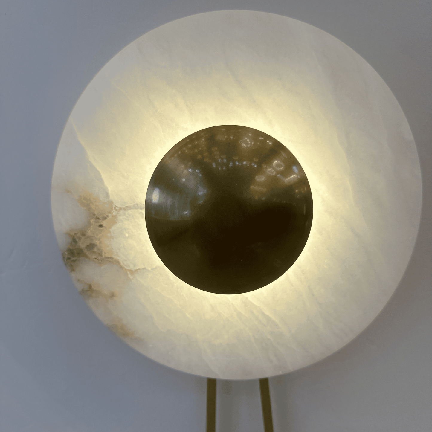 Close-up of alabaster lighting fixture with polished brass disc emitting soft light.