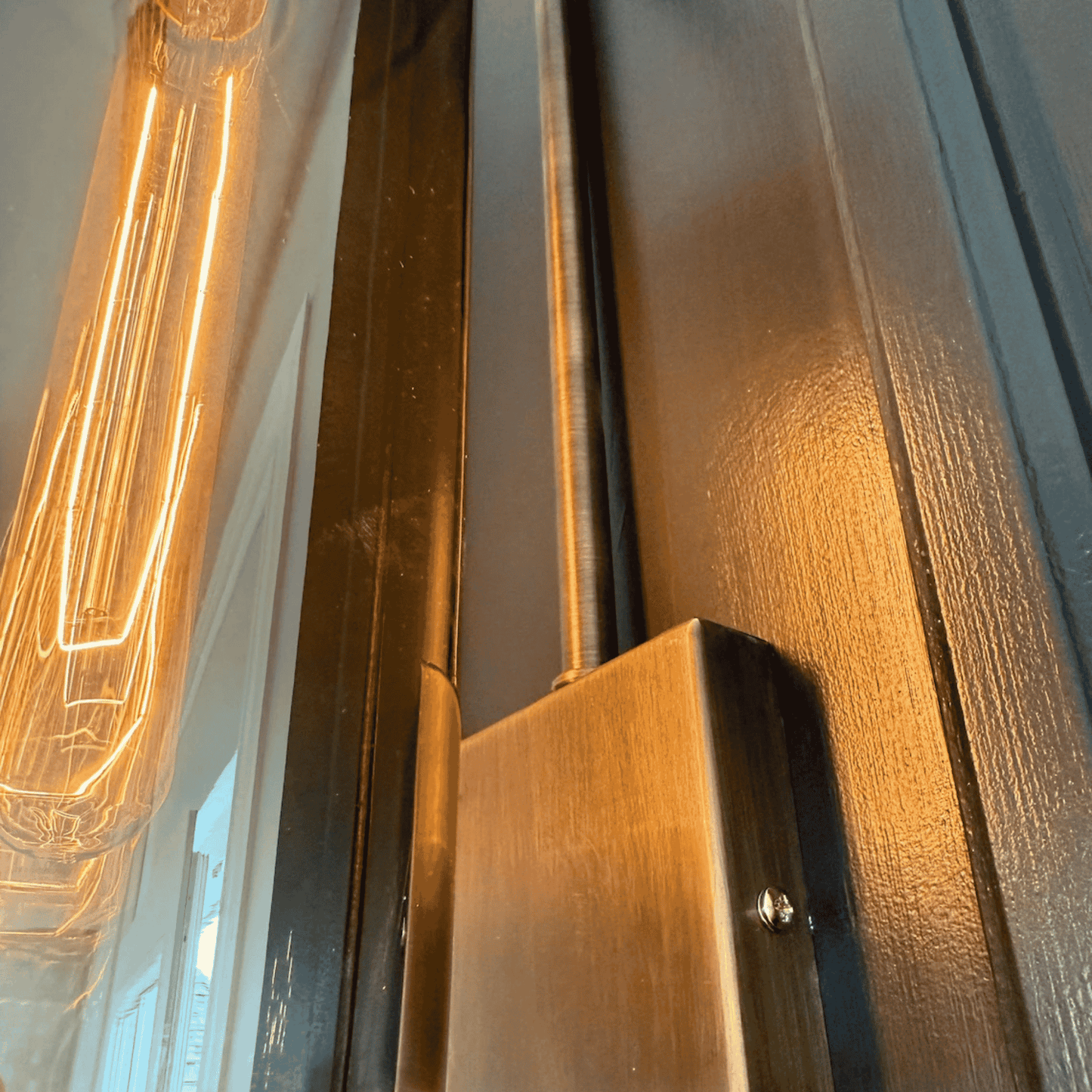 Close-up of blown glass wall sconce showing antique hardware and glowing filament bulb.